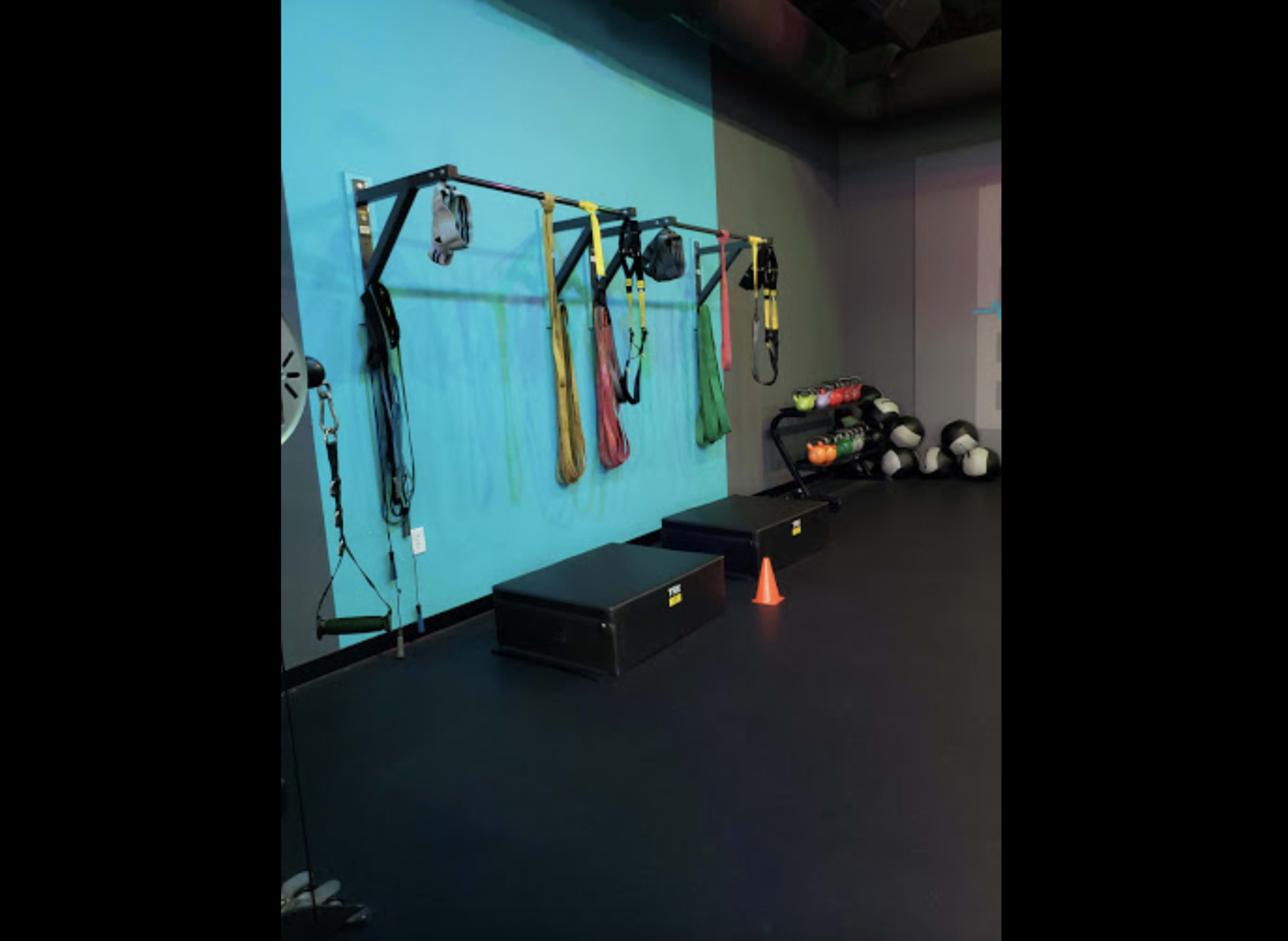 A fitness studio wall with suspension training straps, resistance bands, and two stacked plyometric boxes next to a collection of medicine balls.