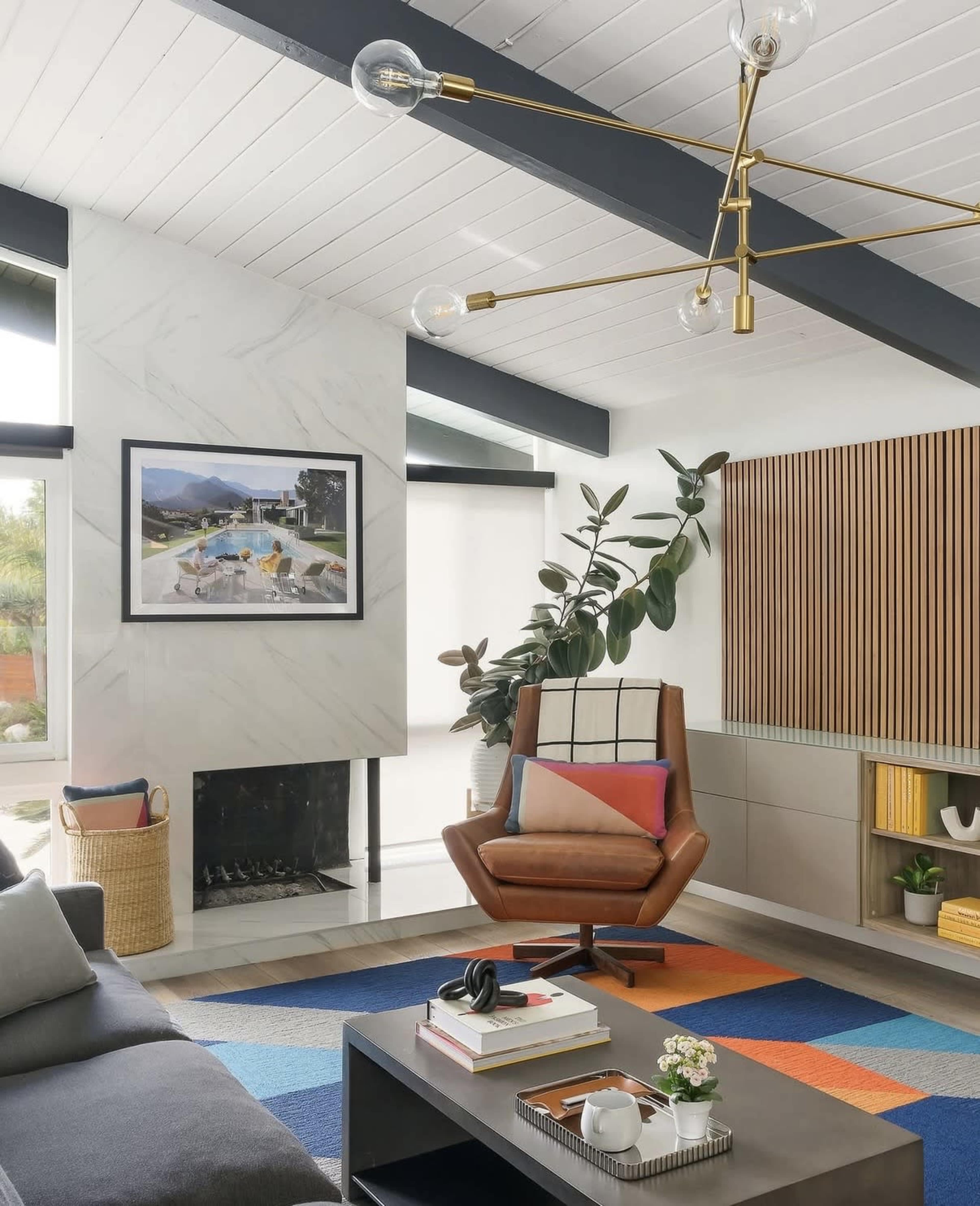 The living room features a modern design with a mid-century armchair, geometric area rug, and a prominent wall art piece above a minimalist fireplace.
