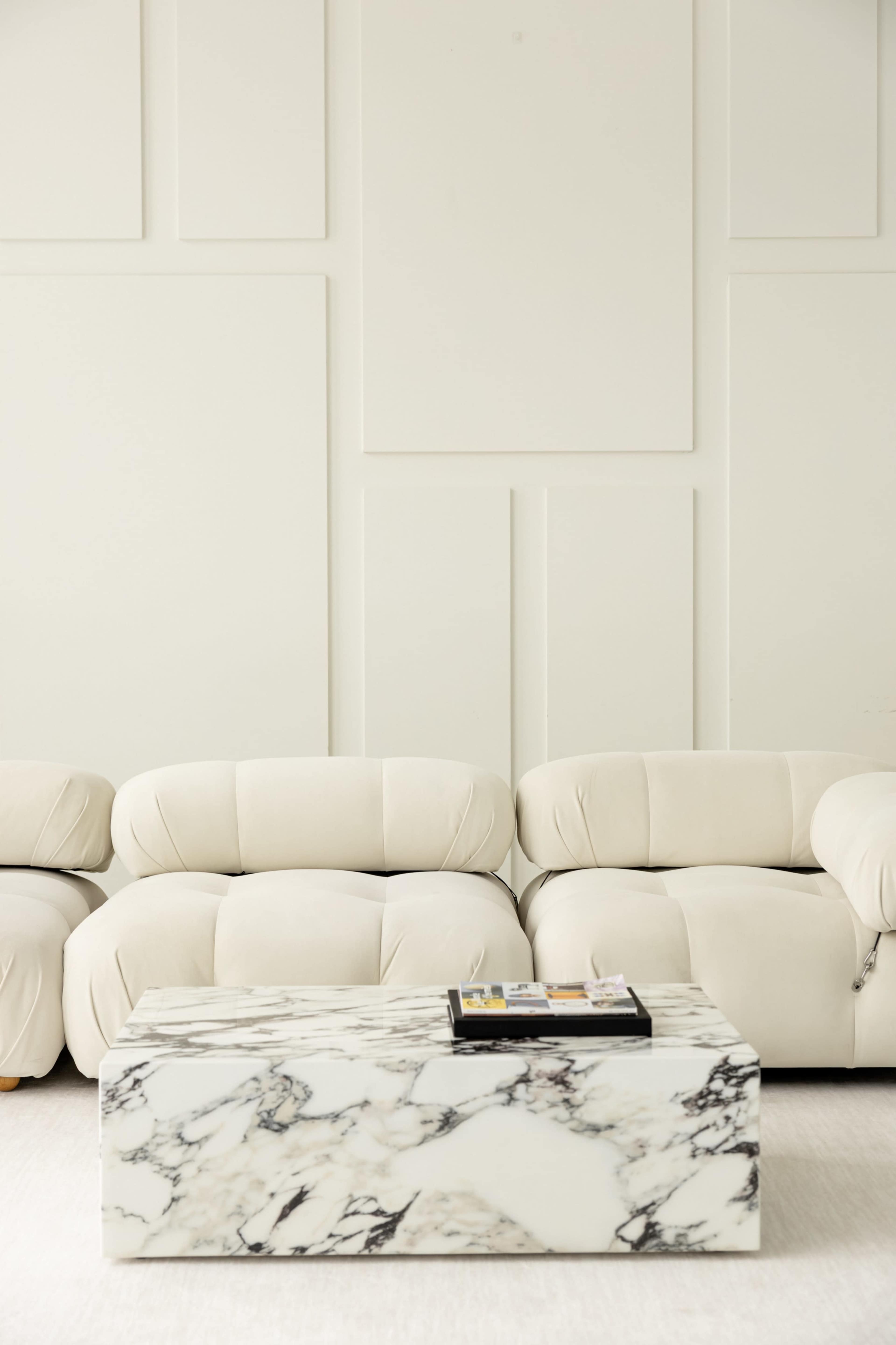 A minimalist living room features a white upholstered sofa and a marble coffee table on a light-colored floor.