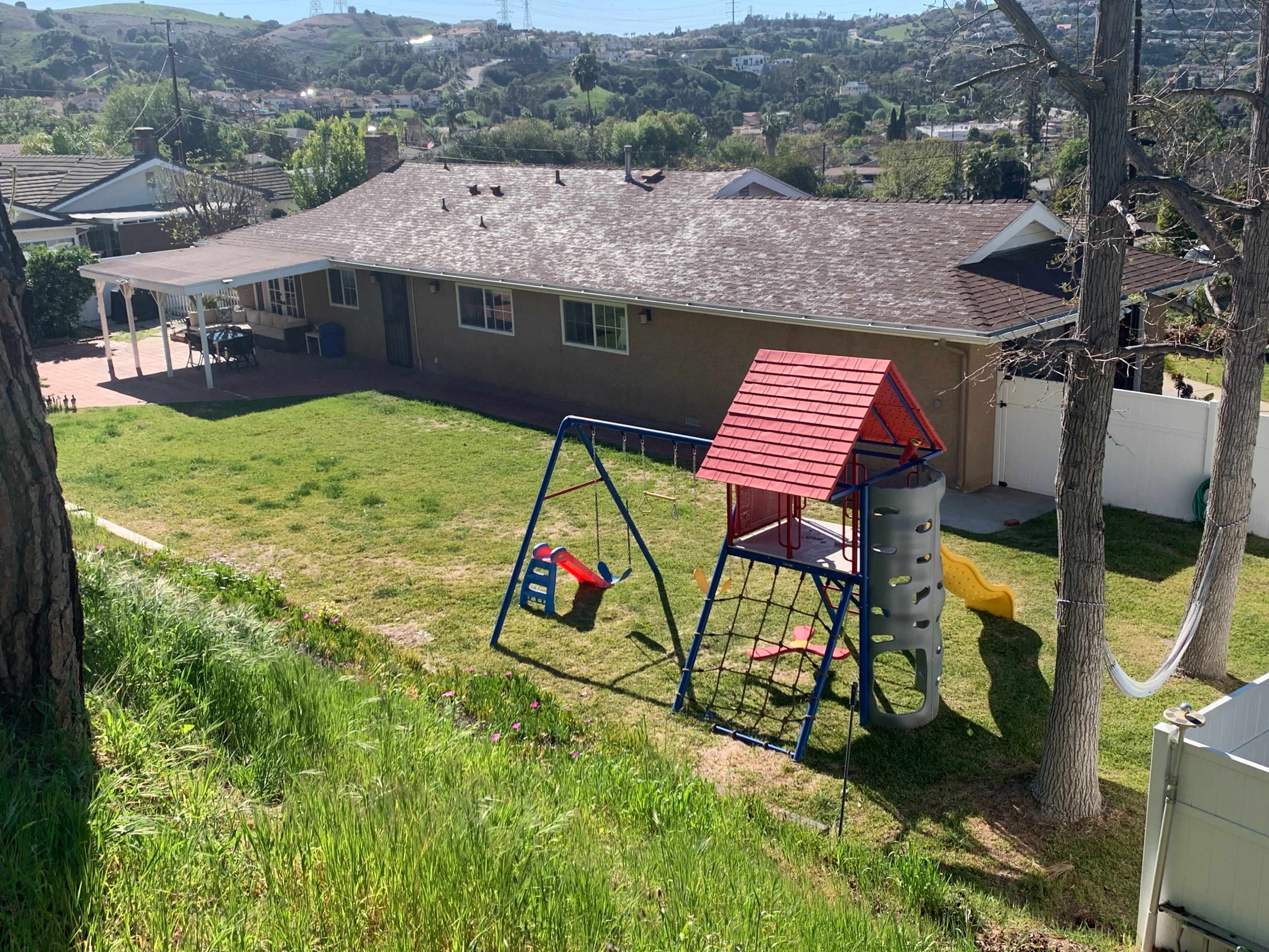 The image shows a backyard with a playground set and a house in the background, surrounded by green grass and trees.