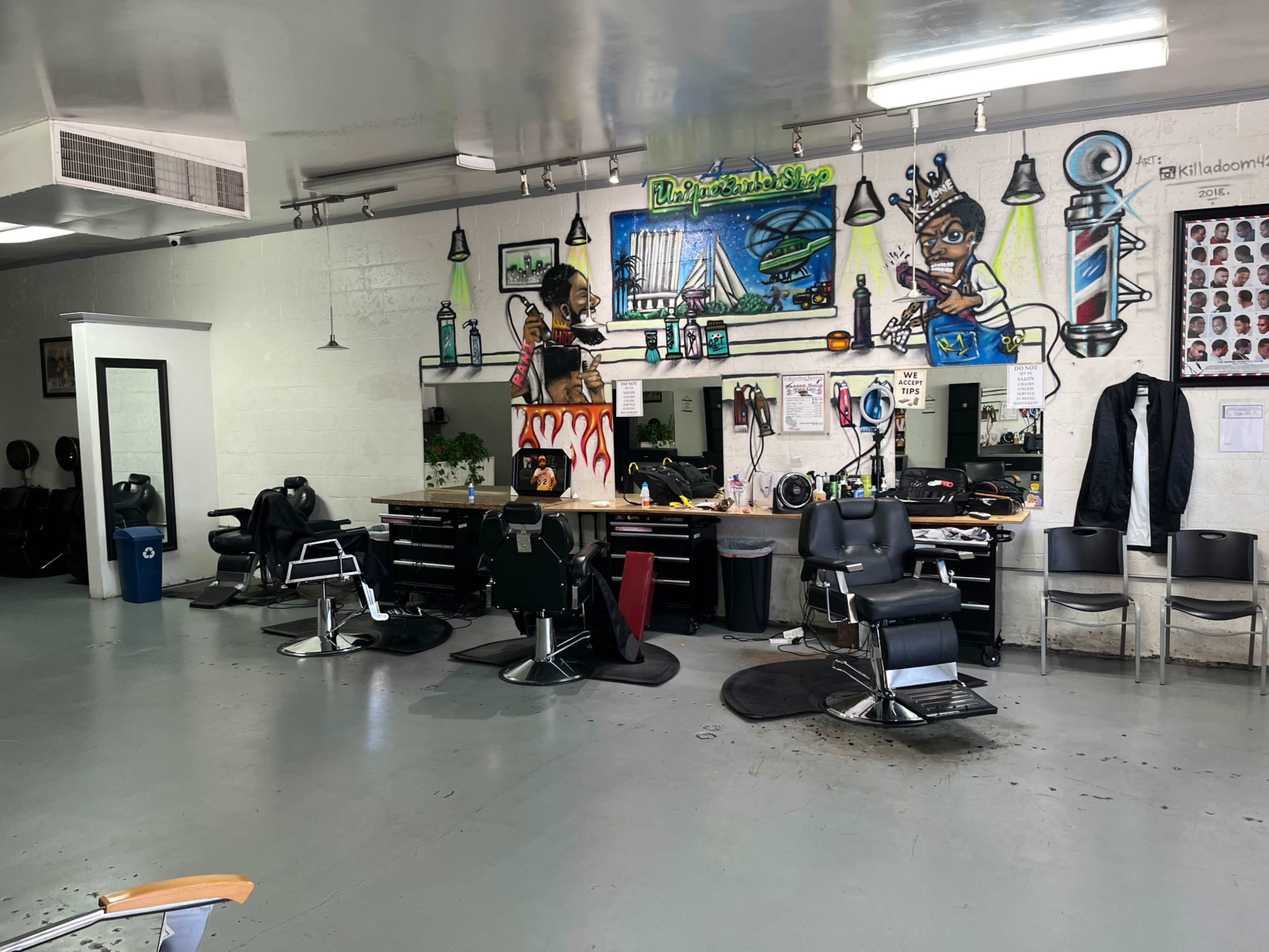 The image shows the interior of a barber shop with several styling chairs, a large mirror, and colorful wall art.