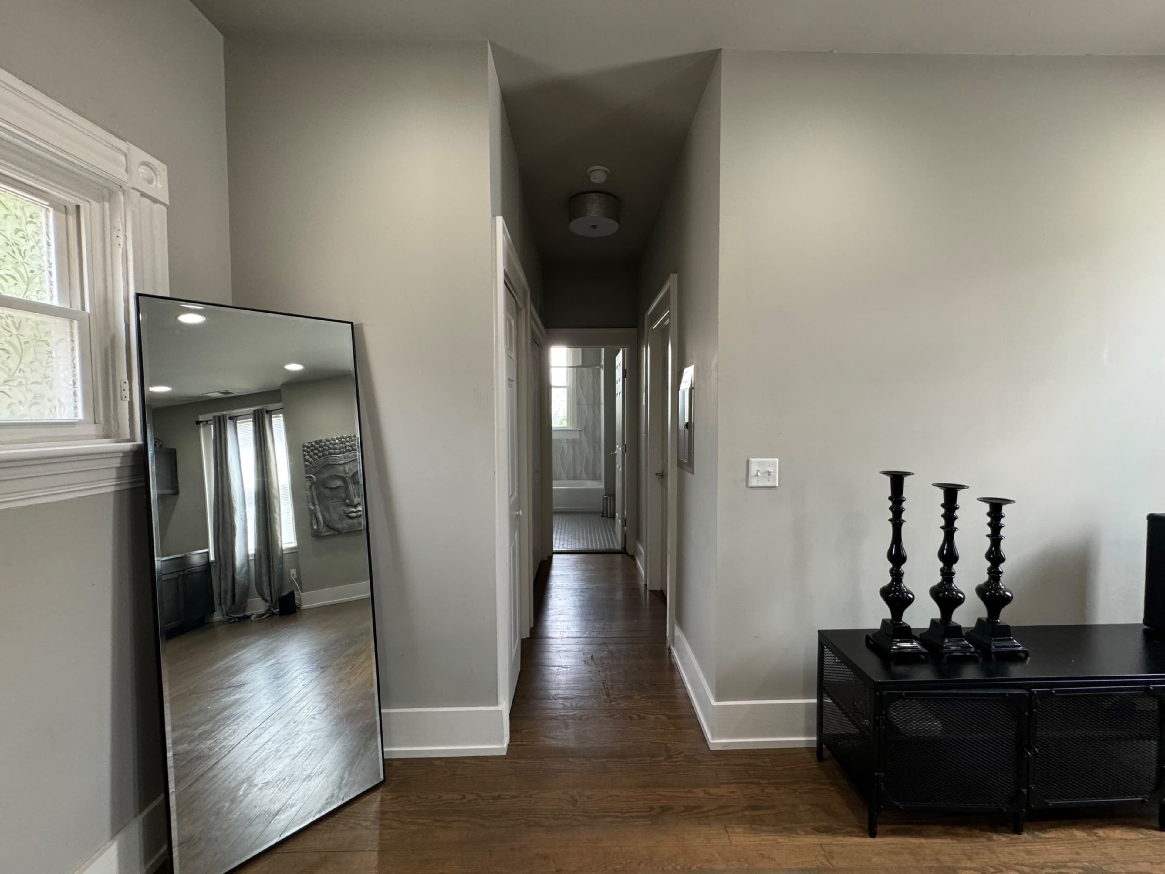 A long hallway is shown, featuring a large mirror on the left, a set of black candlesticks on a table, and a door at the end leading to another room.