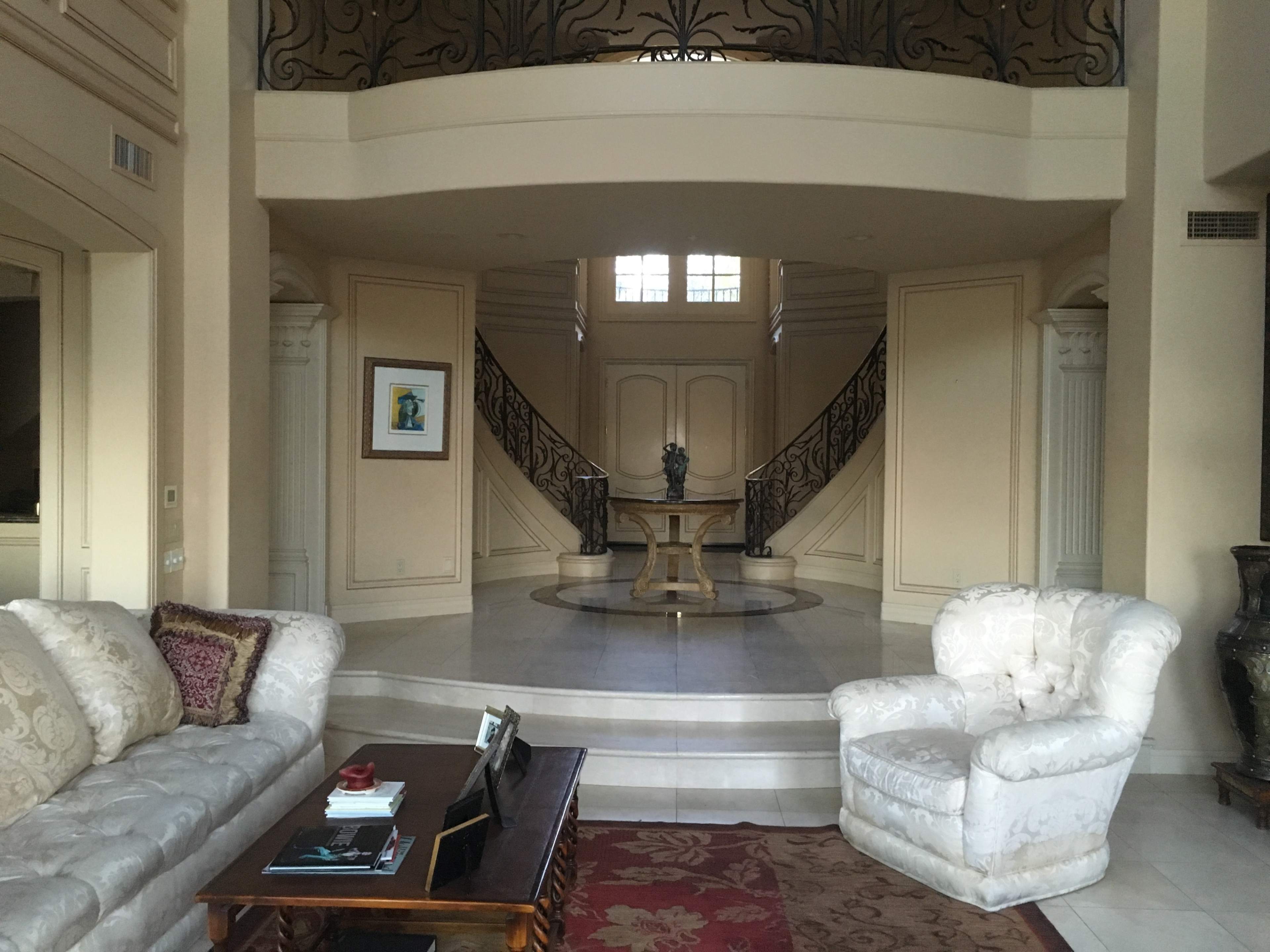 A spacious entryway featuring a marble floor, a round table, and a staircase with decorative railings leading to an upper level.