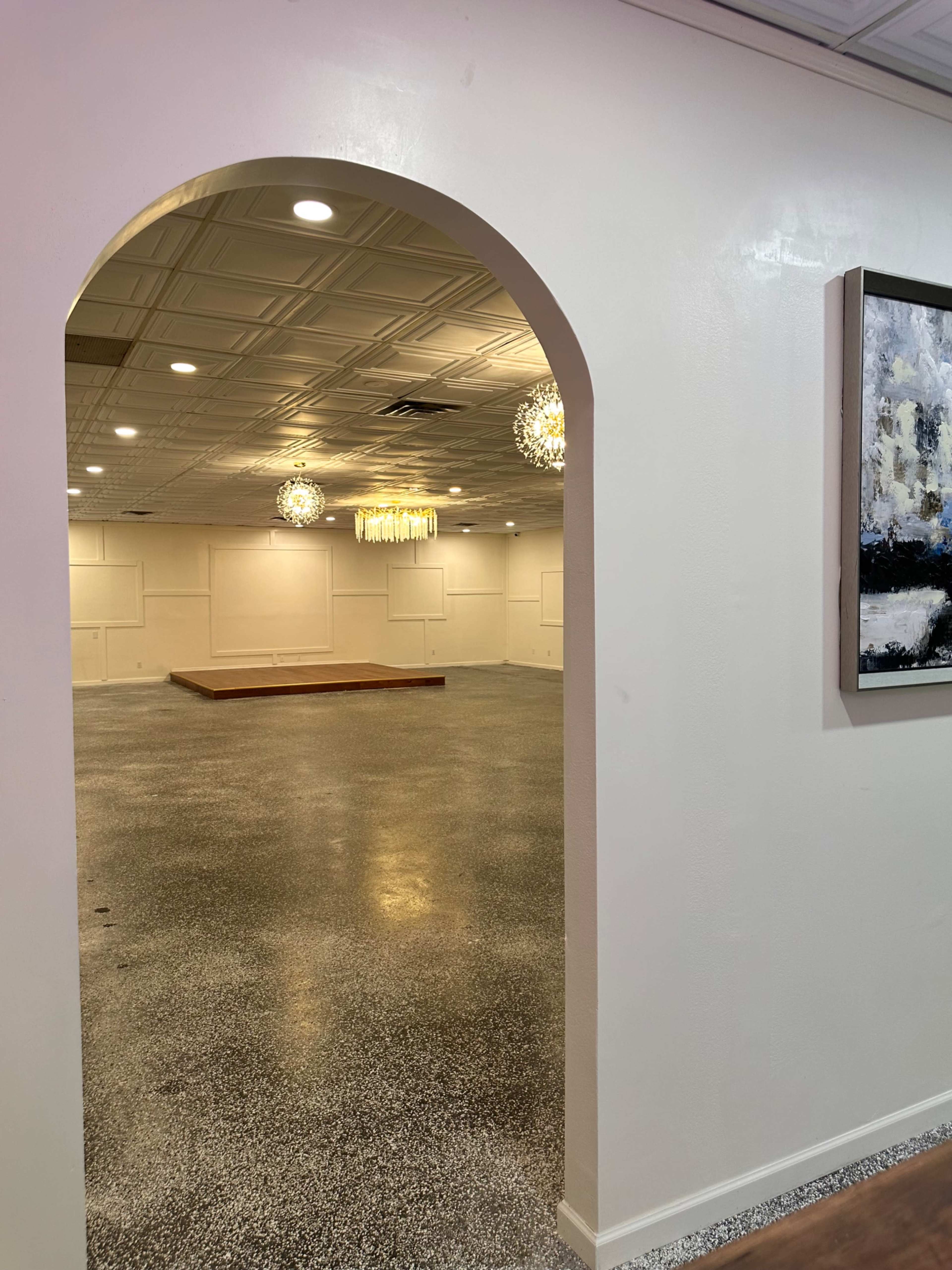 An arched entryway leading into an empty event hall with a polished floor and subtle overhead lighting.