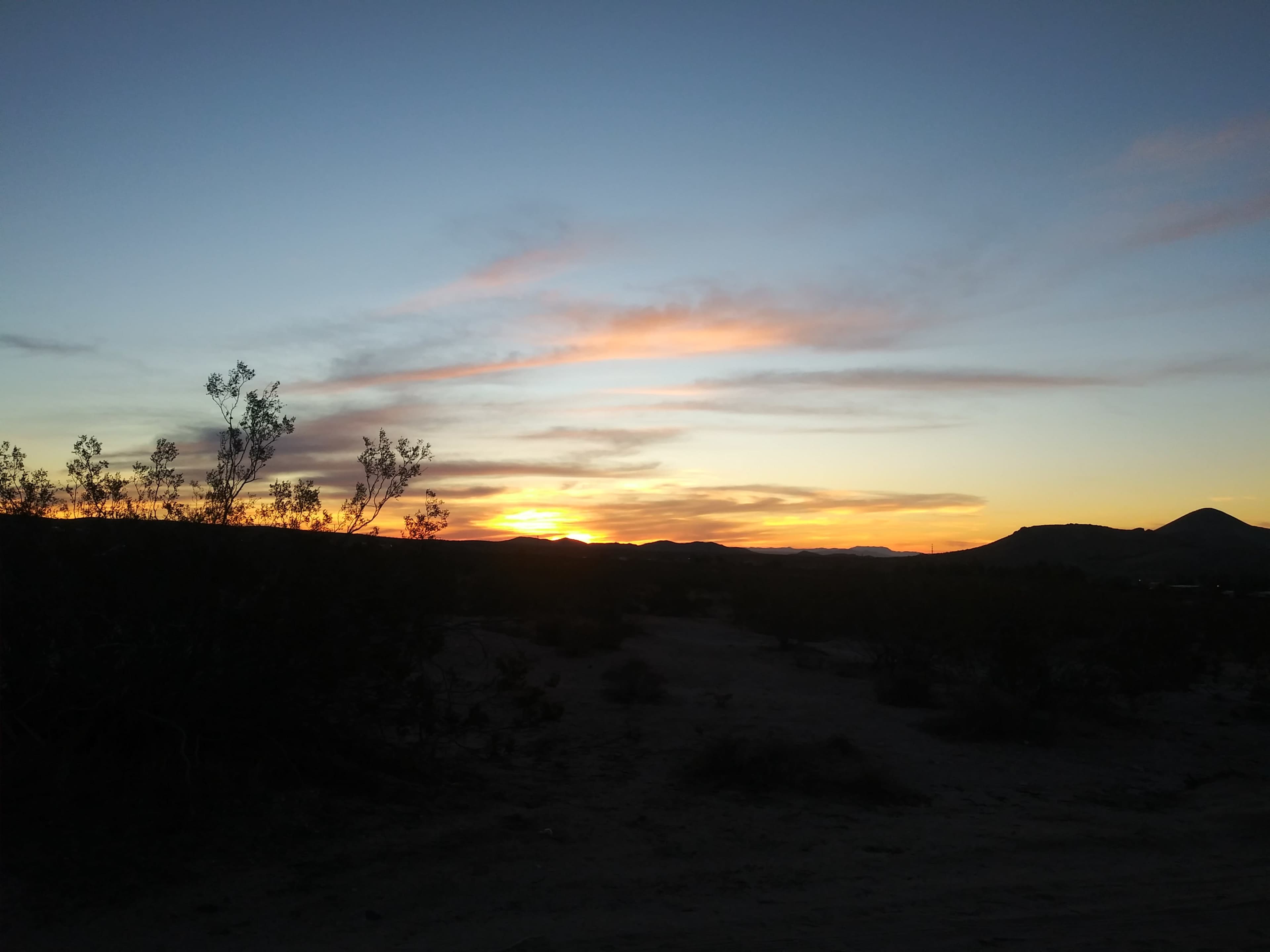 The sun sets behind distant hills, casting a gradient of colors against the sky.