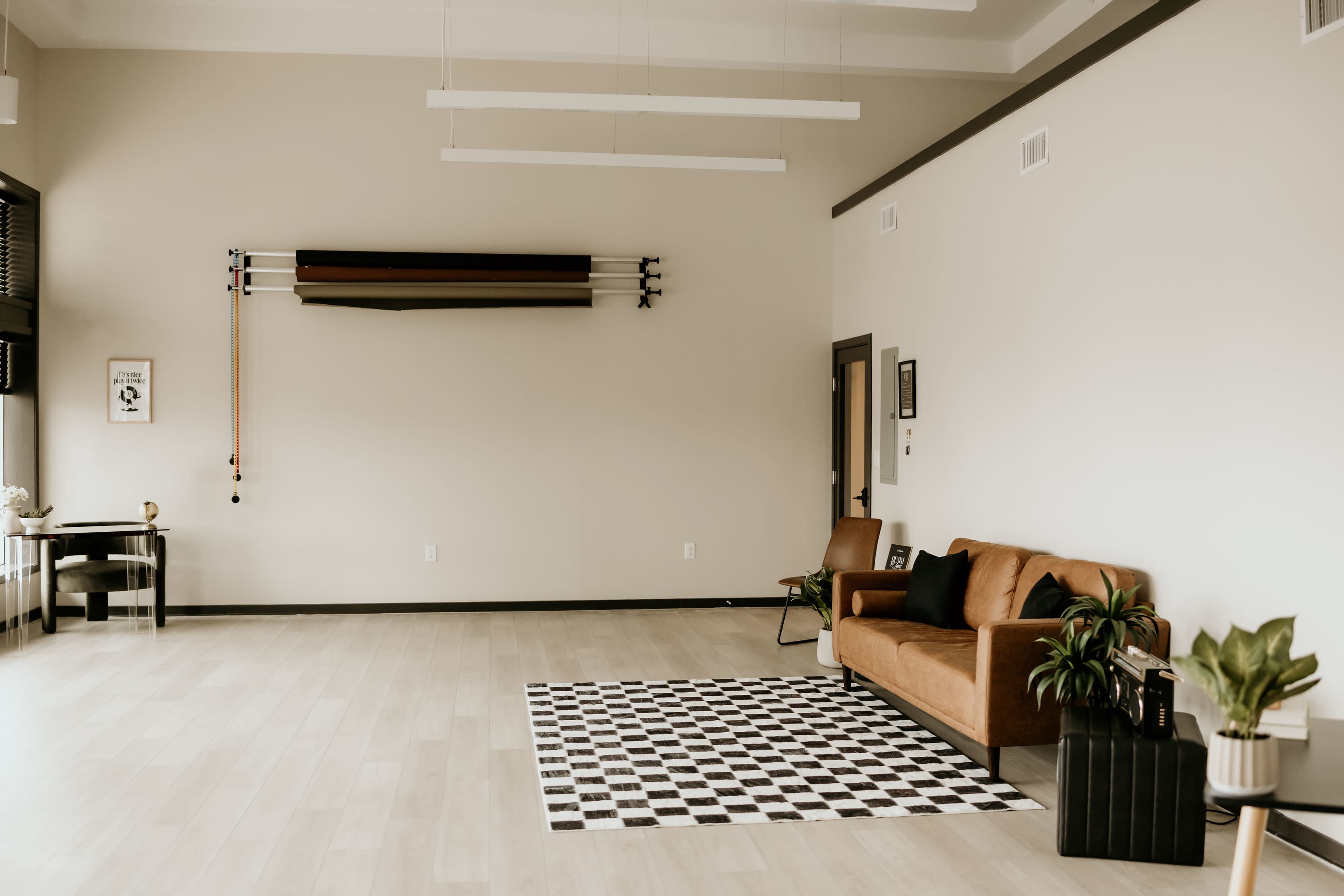 A spacious, minimalistic room features a brown sofa, a checkered rug, and wall-mounted decorative items.
