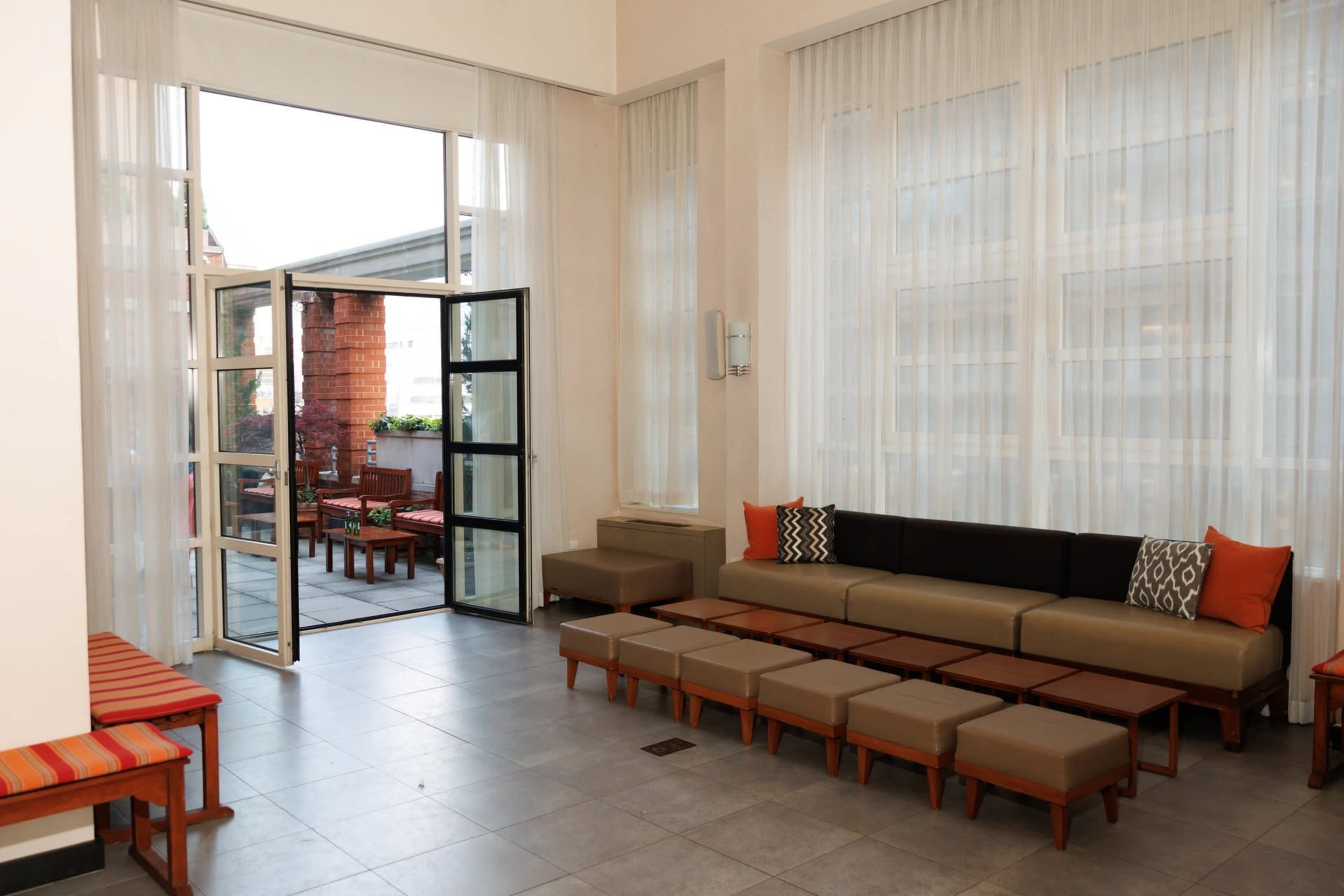 The image shows a bright, modern lounge area with a large seating arrangement and an open door leading to an outdoor space.