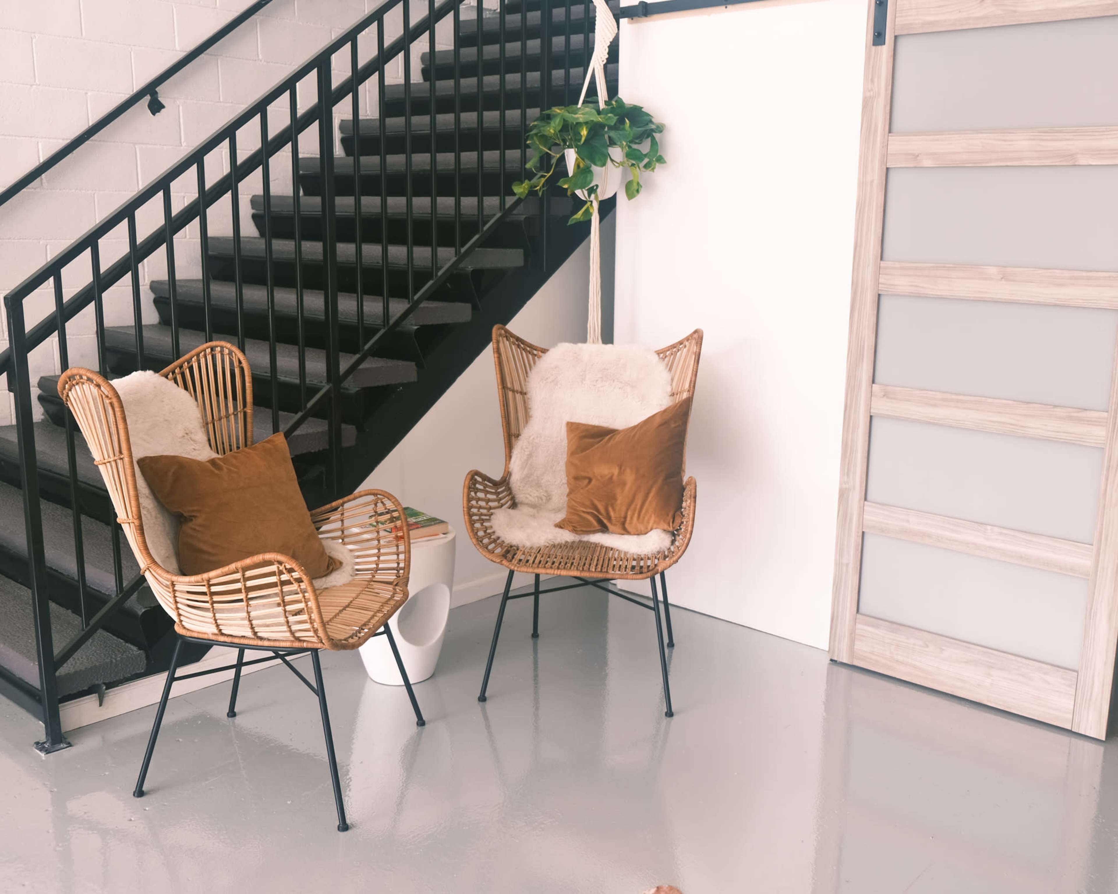 A small seating area with two rattan chairs and a potted plant near a staircase and a sliding door.