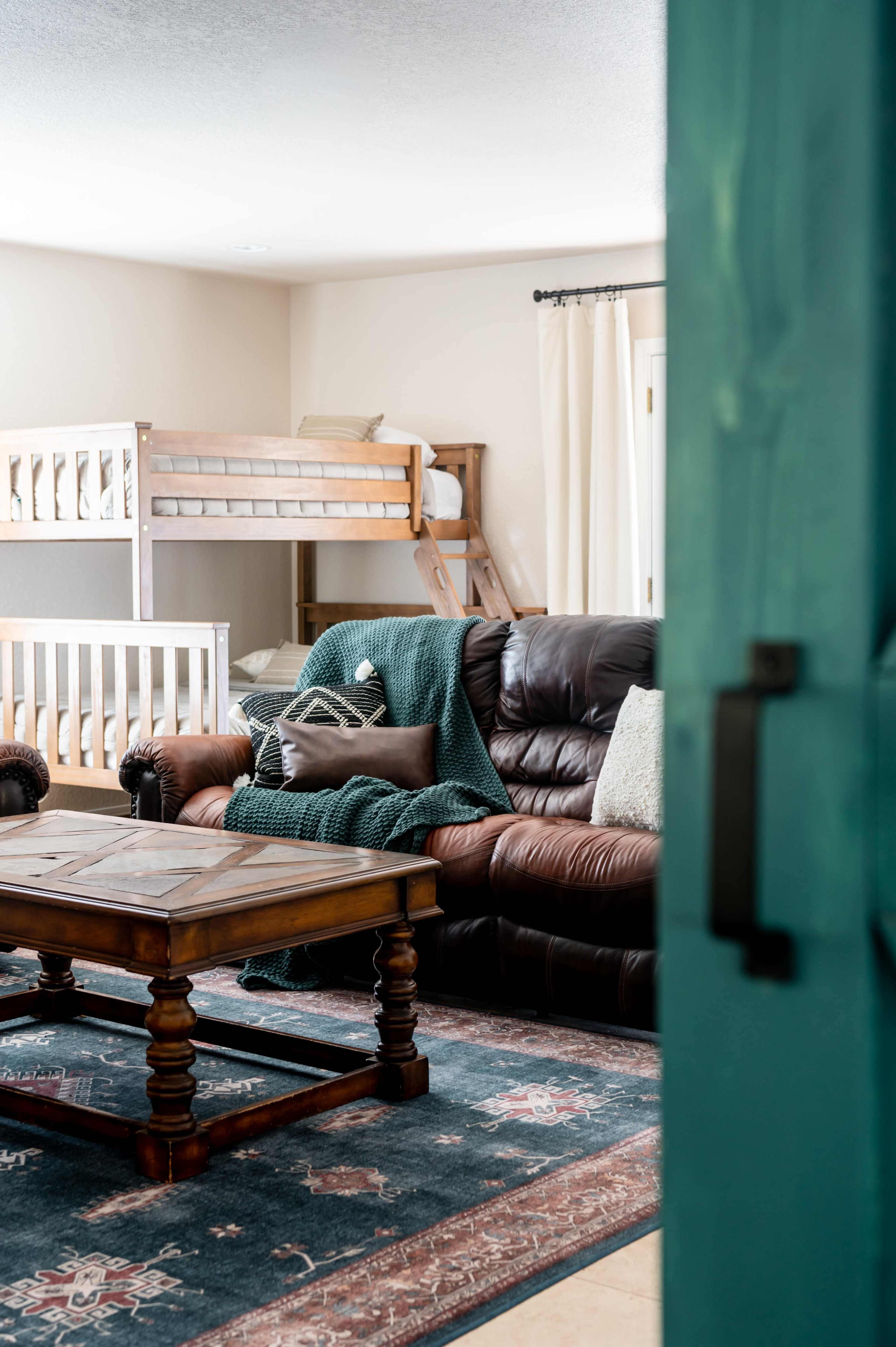 A living room with a brown leather sofa, a wooden coffee table, and a bunk bed in the background.