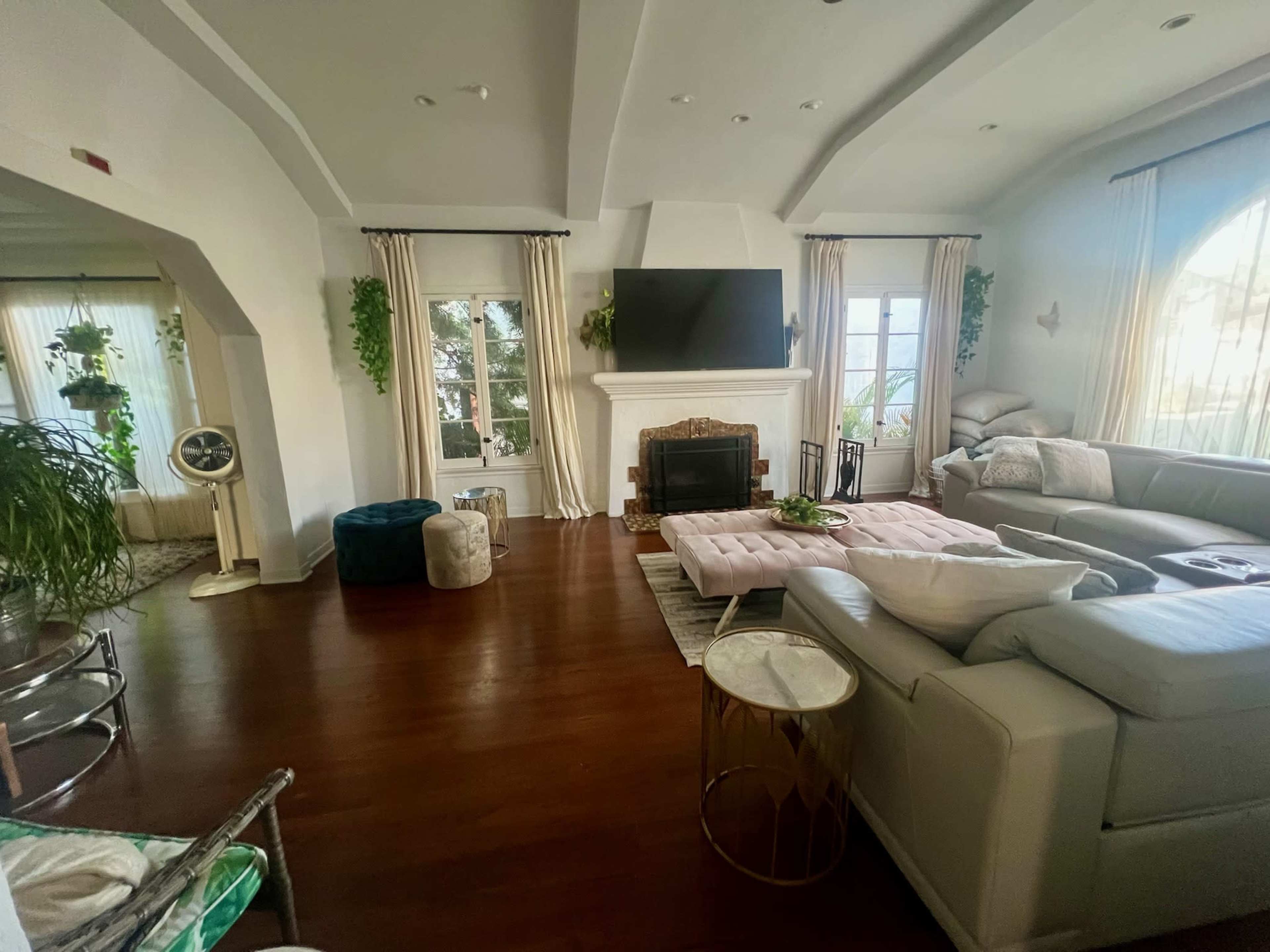 The image shows a spacious living room with a fireplace, large windows, and modern furniture arranged around a central seating area.