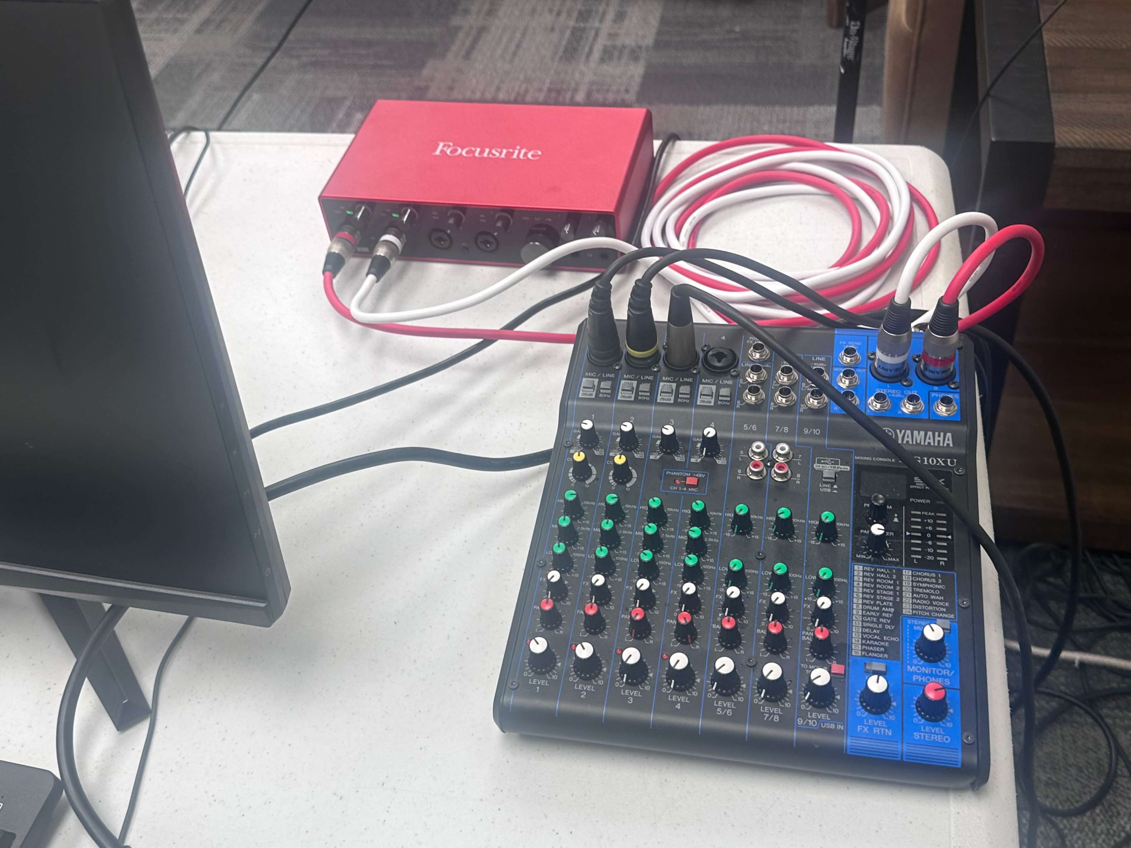 The image shows a Yamaha audio mixer connected to a Focusrite audio interface, with various input cables and a monitor on the side.