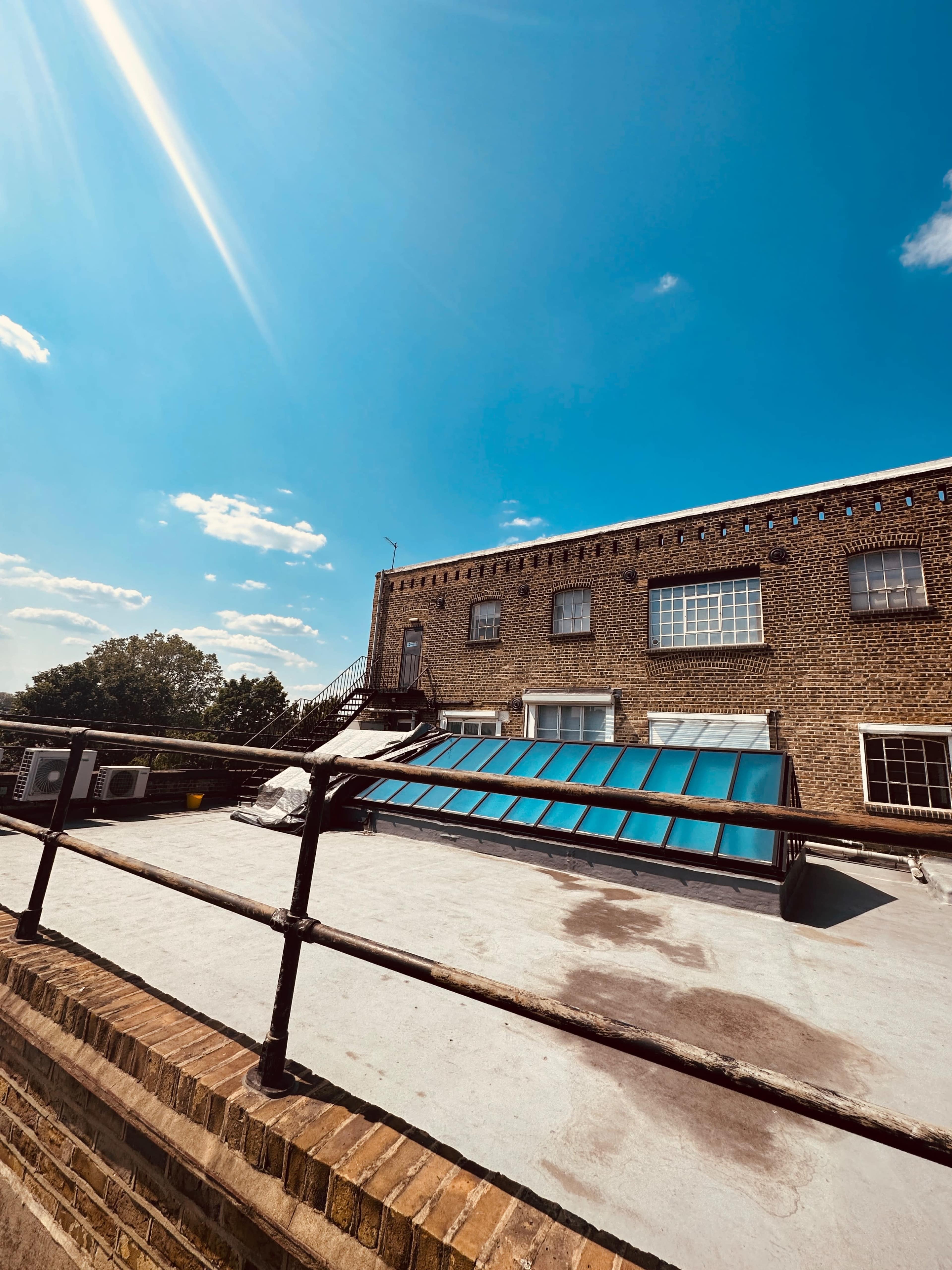 A rooftop area of a brick building with several skylights and railings under a blue sky.