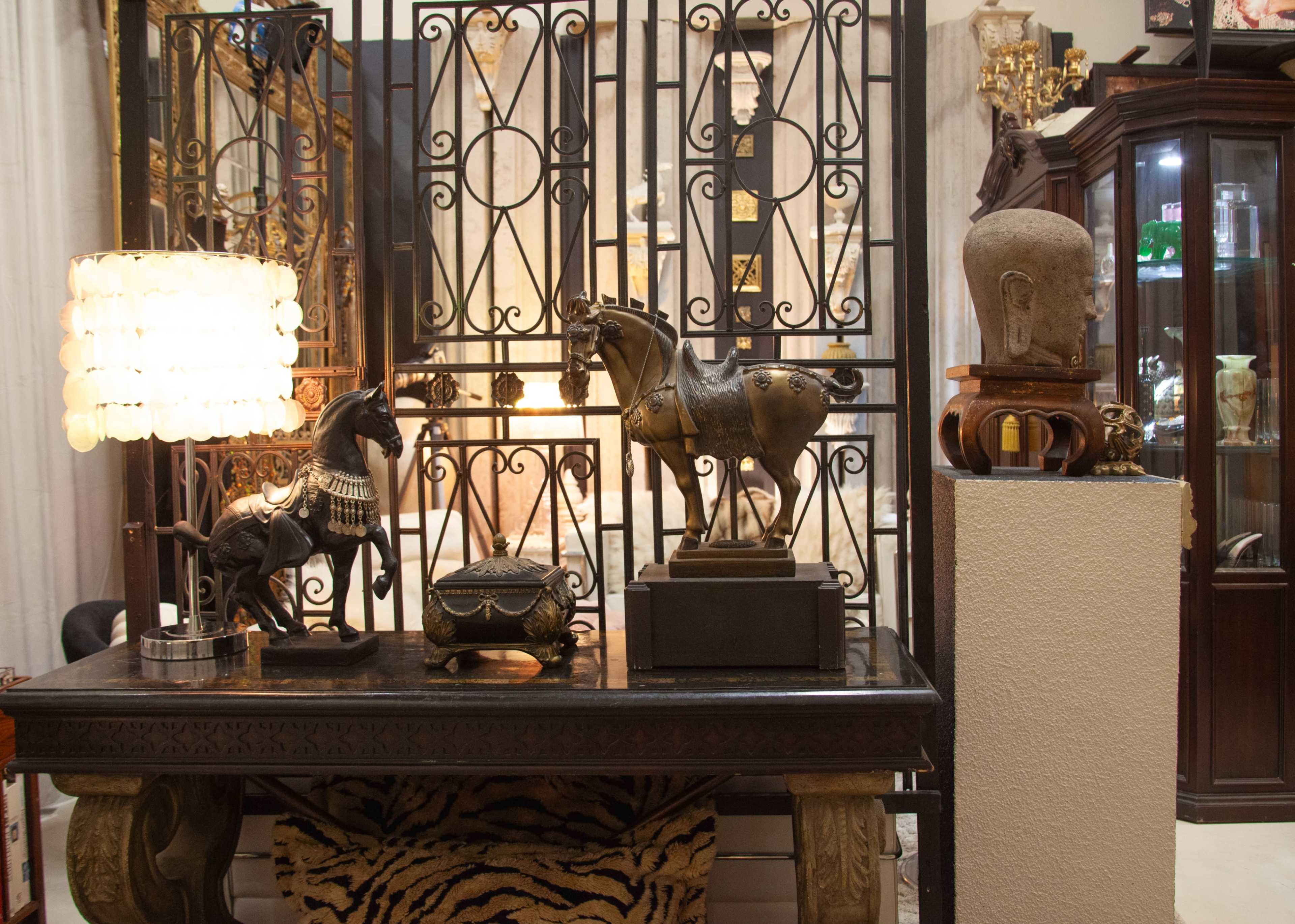 The image shows a table displaying various decorative items, including horse sculptures, an ornate lamp, and a cabinet in the background filled with glass artifacts.