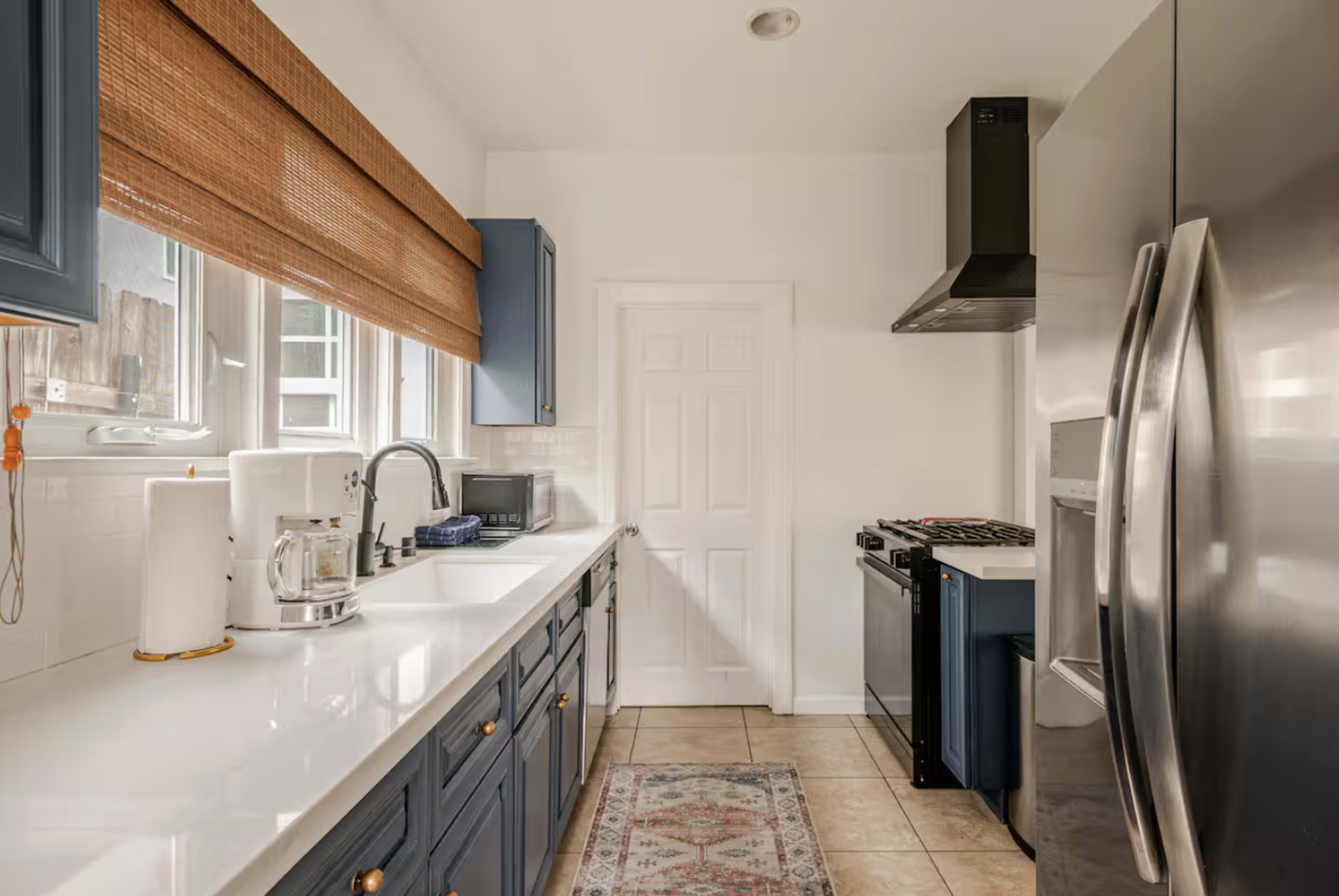 The kitchen features blue cabinetry, a double-basin sink, stainless steel appliances, and a window with a bamboo shade.