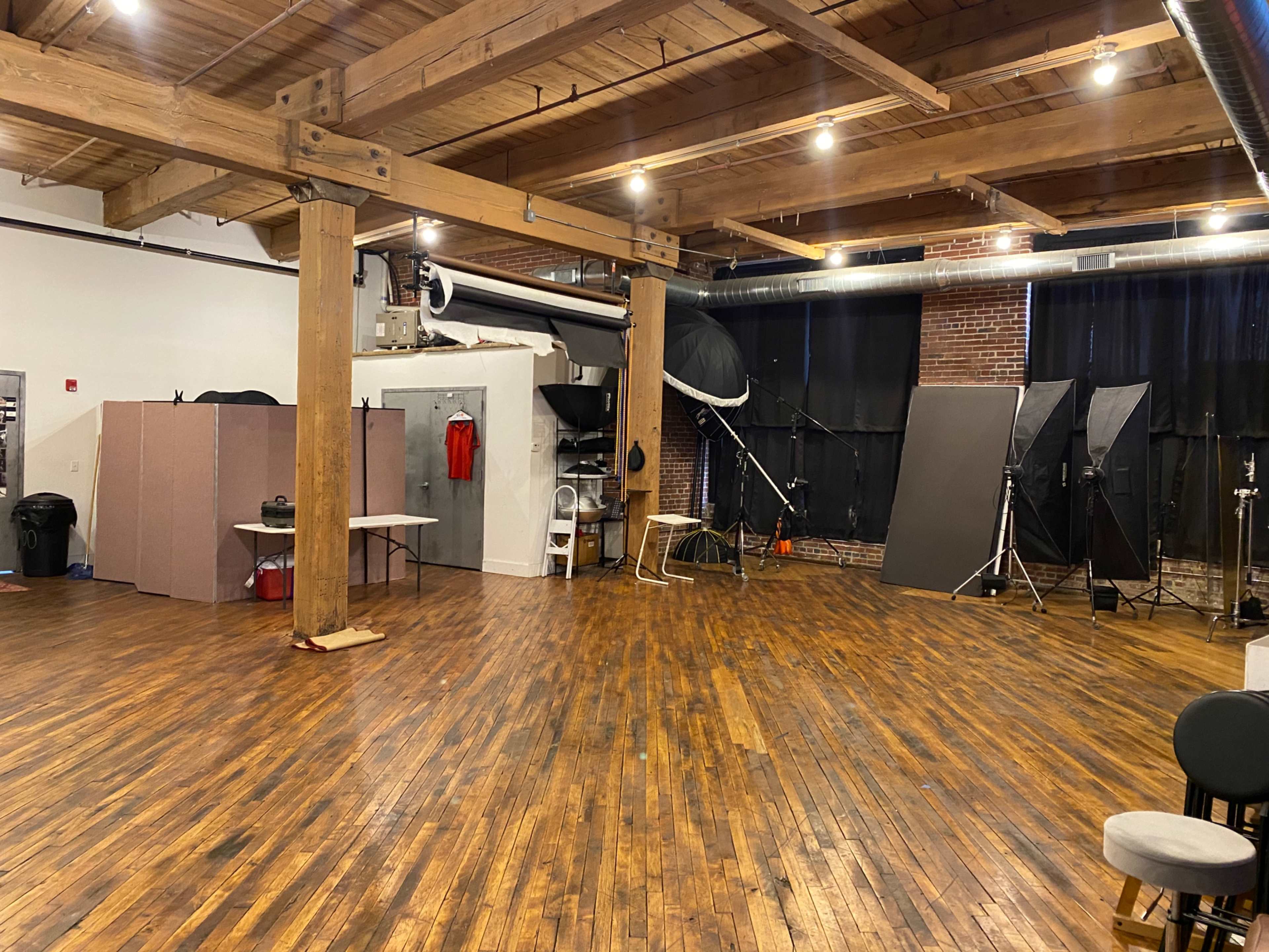 An empty photography studio featuring wooden floors, exposed beams, and various equipment positioned around the space.
