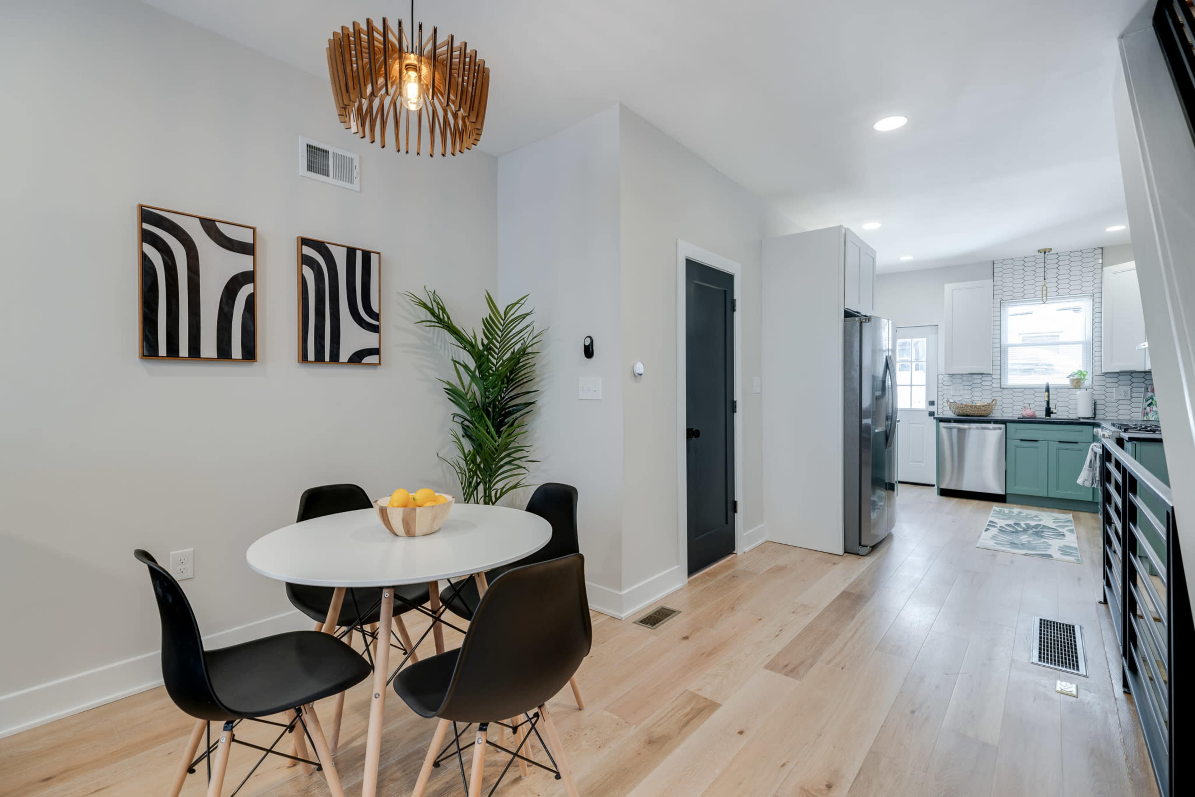A dining area features a round table with four black chairs, accompanied by two abstract wall art pieces and a pendant light above.