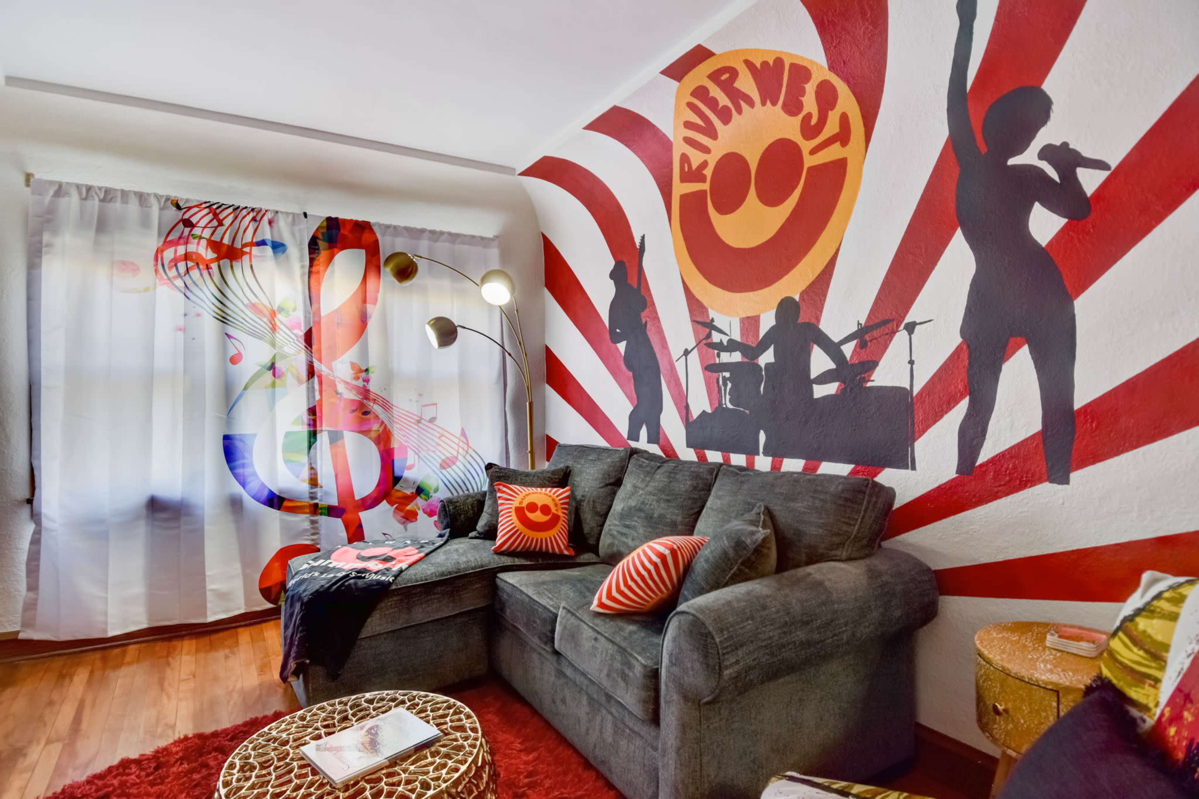 A vibrant living room featuring a gray sofa, colorful wall murals of musical notes and figures, and a decorative rug.