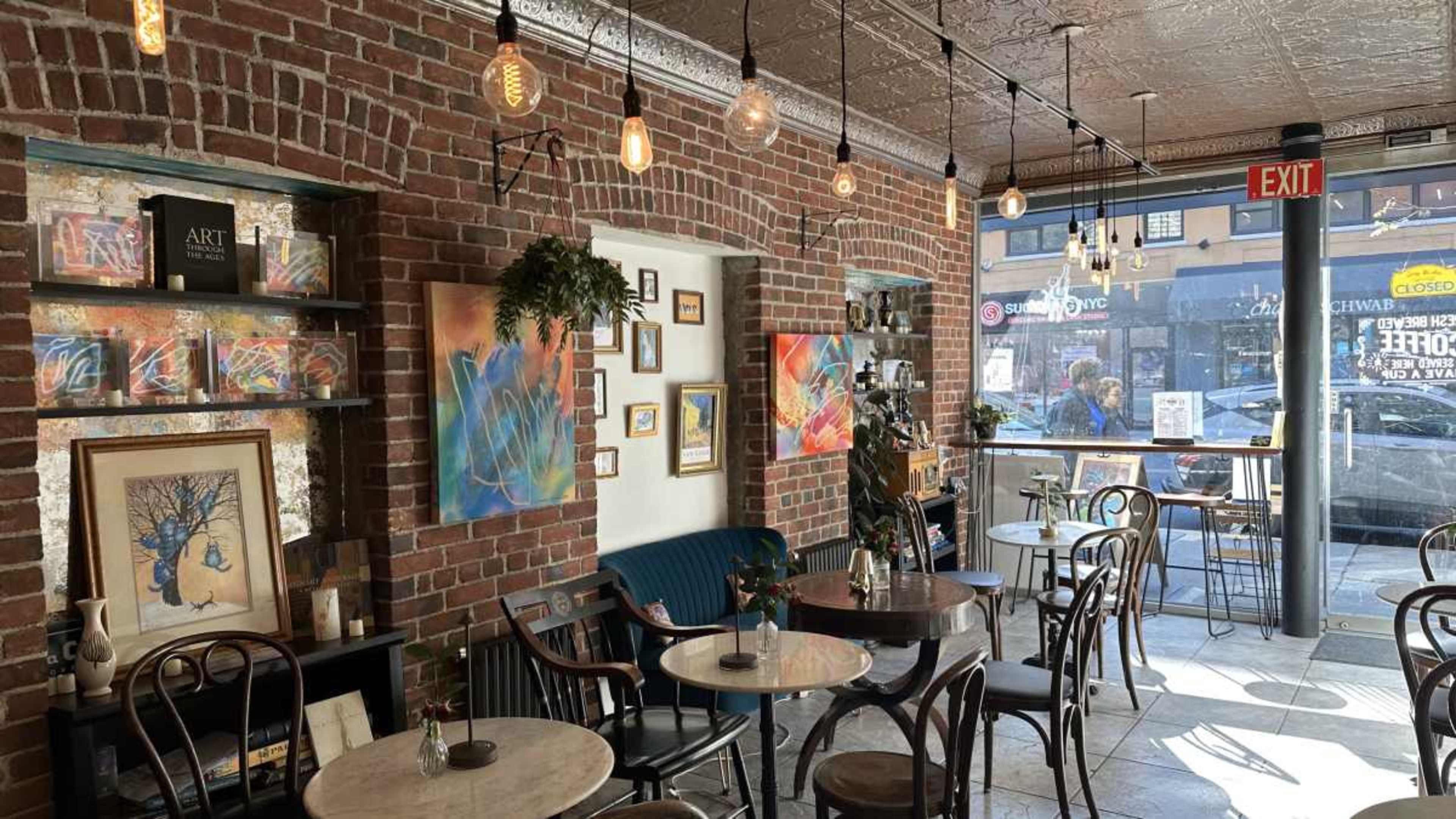 A cozy coffee shop interior with exposed brick walls, small marble tables, and colorful artwork displayed on the walls.