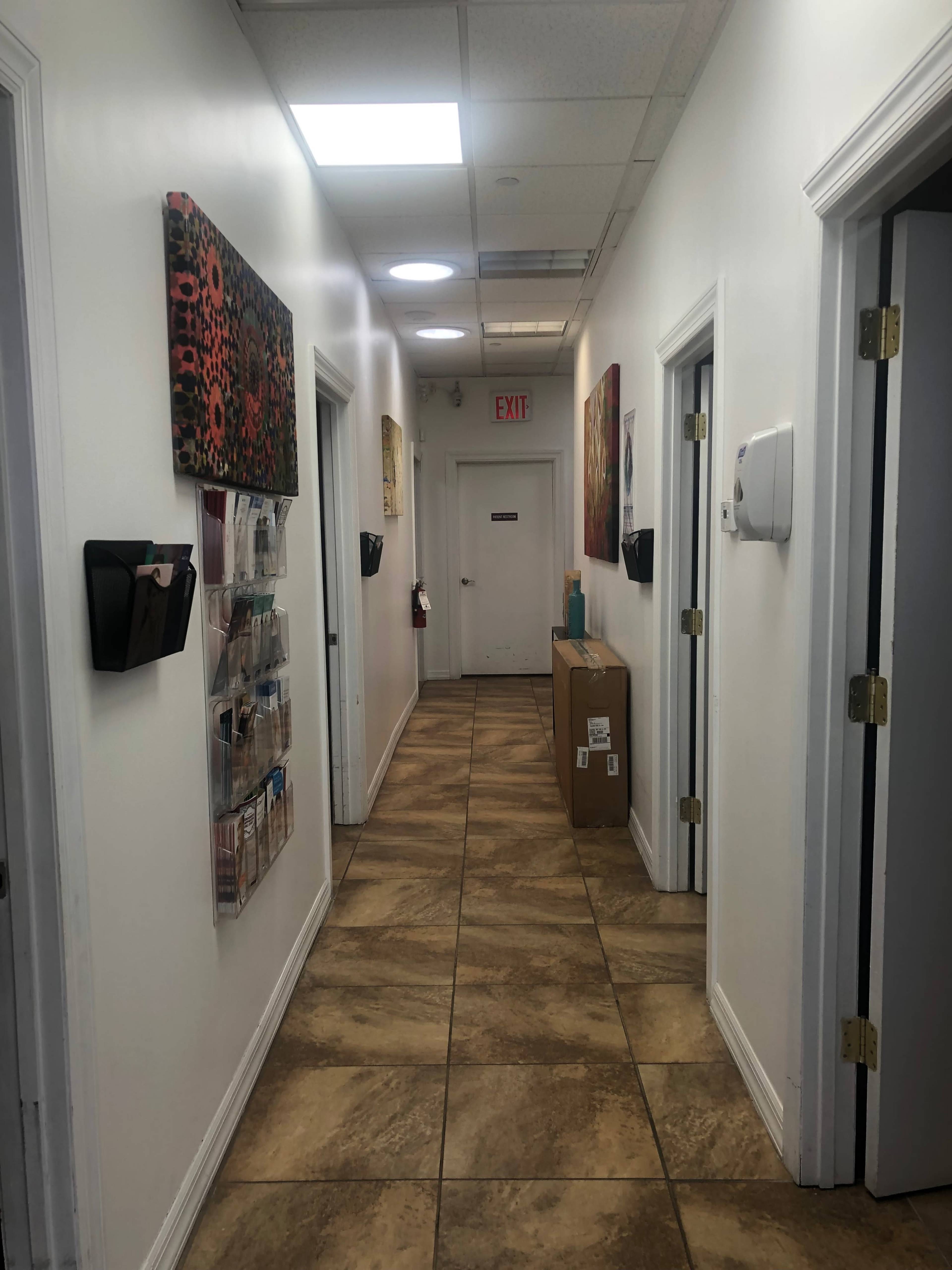 The image shows a long hallway with doors on either side, decorated with artwork, and features a brown package near the end of the corridor.
