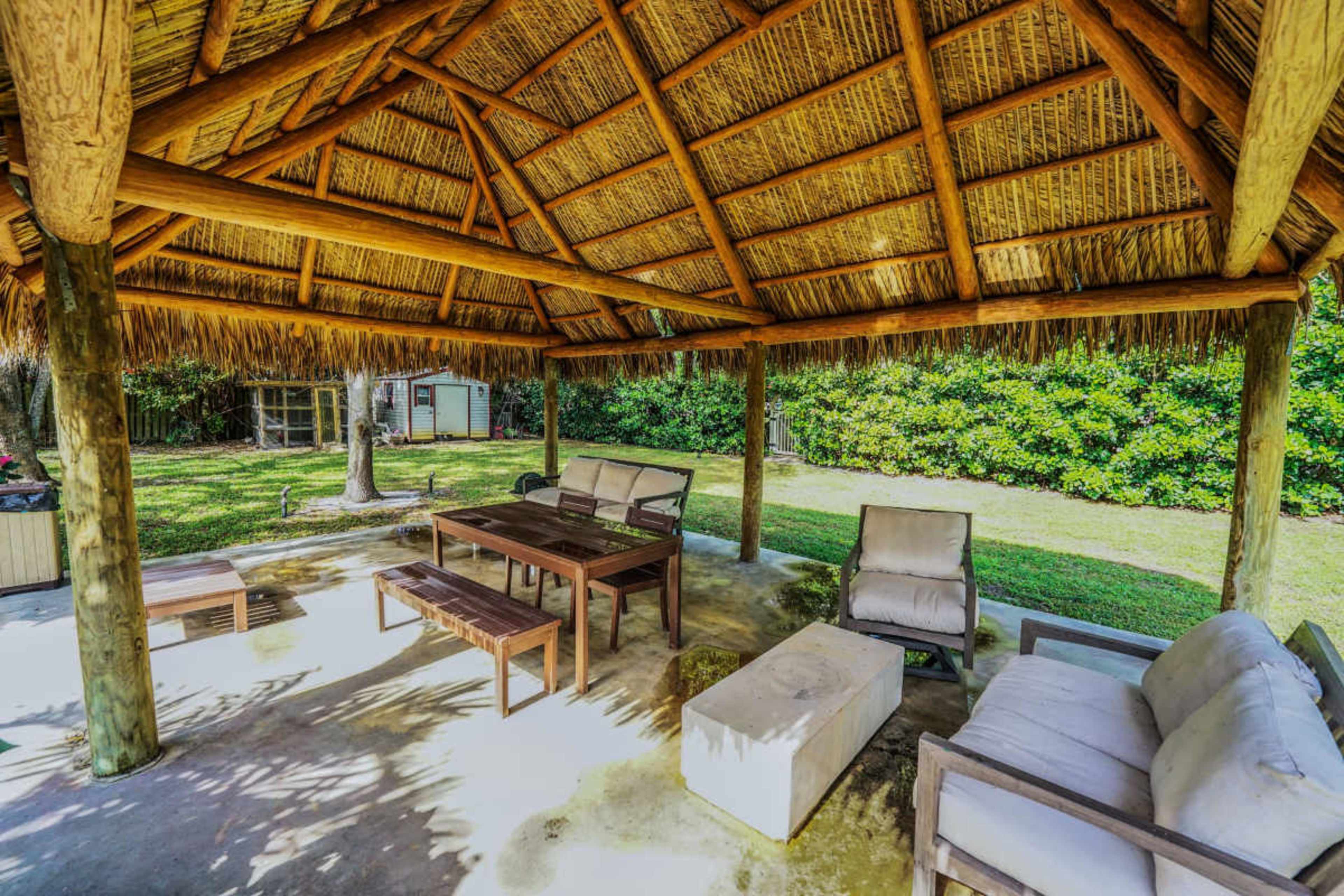 The image shows a shaded outdoor seating area featuring wooden furniture and a thatched roof.
