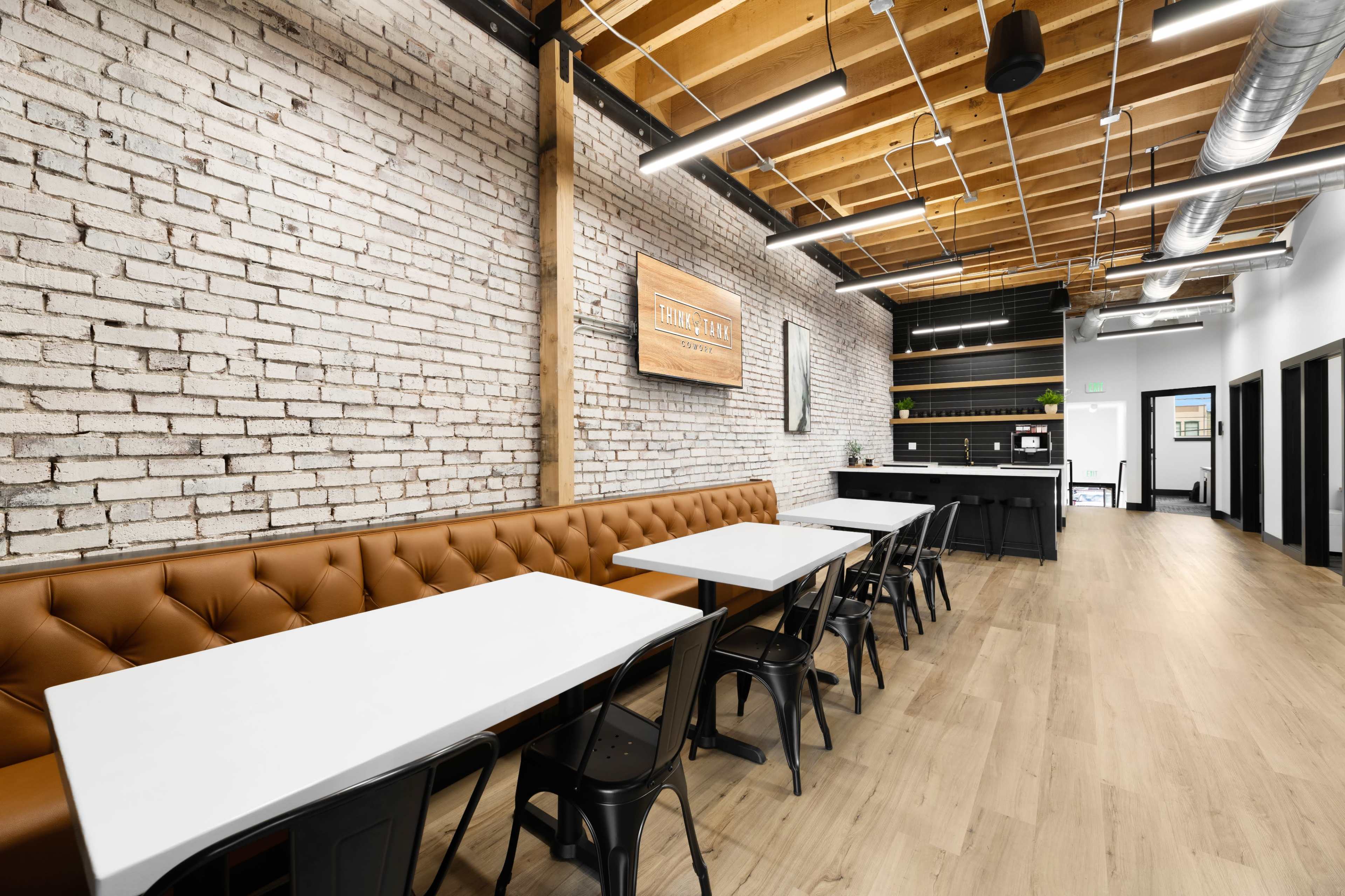 A modern dining area with white tables, black chairs, a brick wall, and wooden beams in a well-lit space.