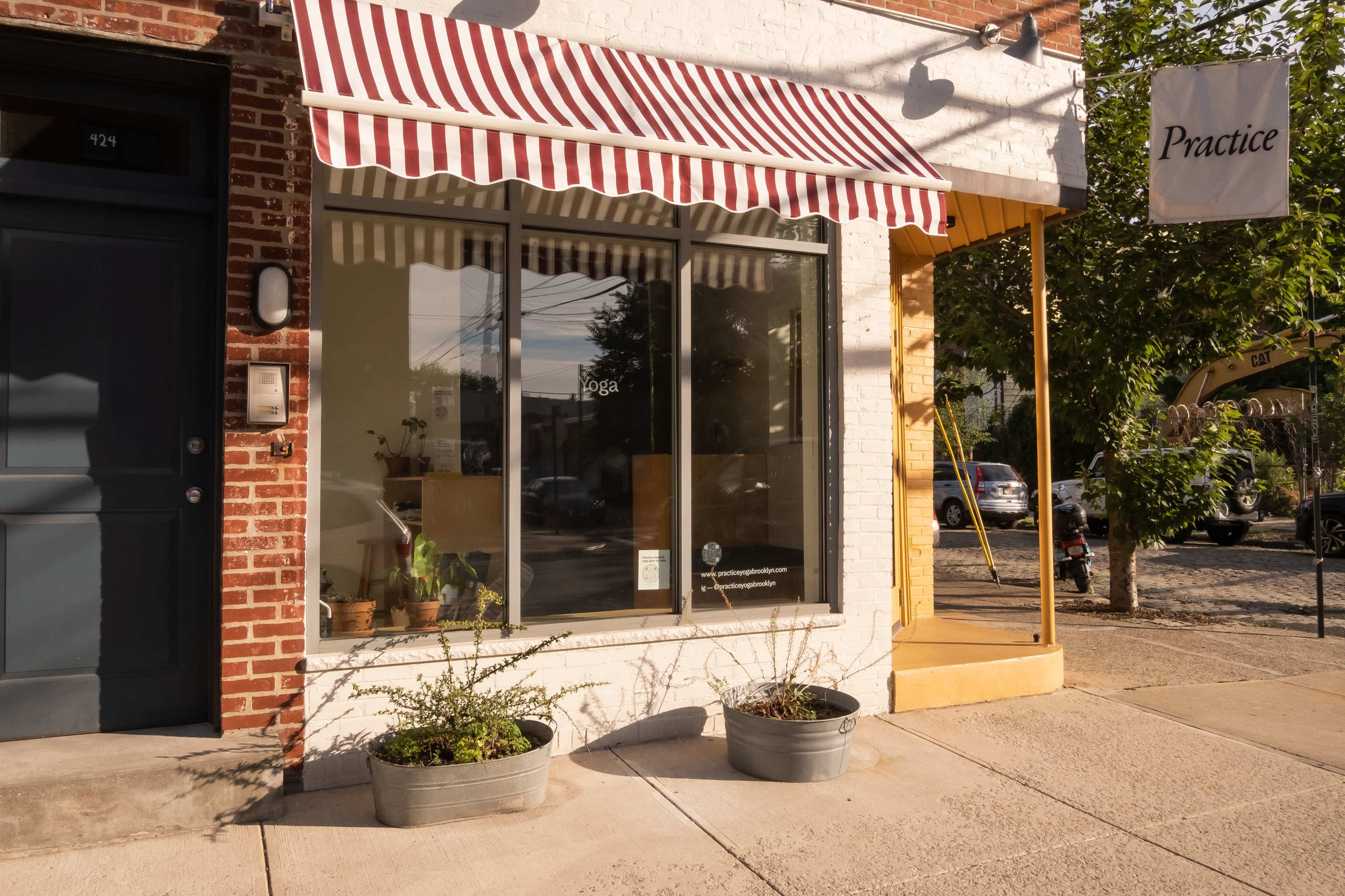 A storefront with striped awnings, potted plants on the sidewalk, and a sign that reads "Practice."