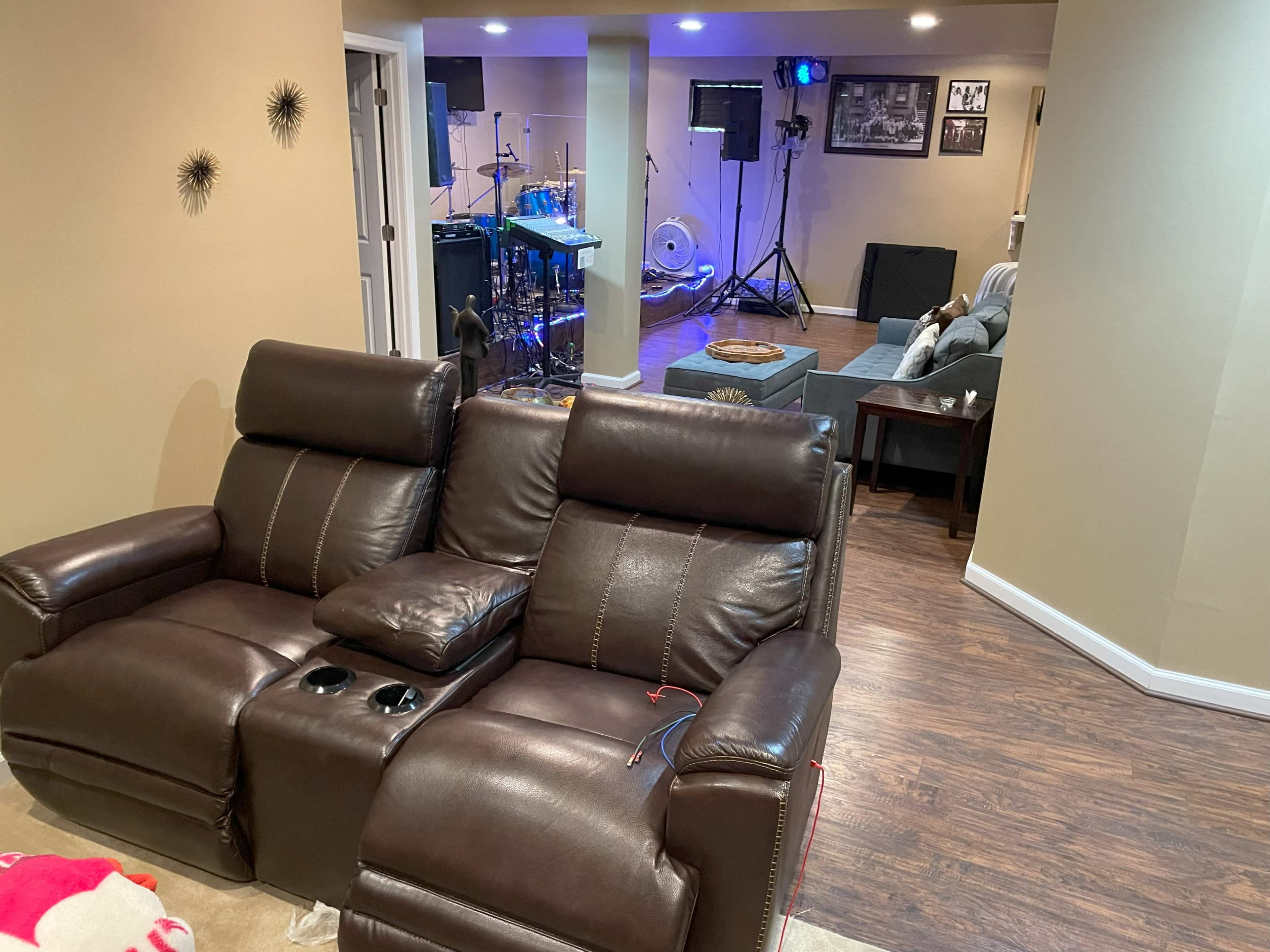 A spacious basement with a brown leather reclining sofa in the foreground and a band setup in the background.