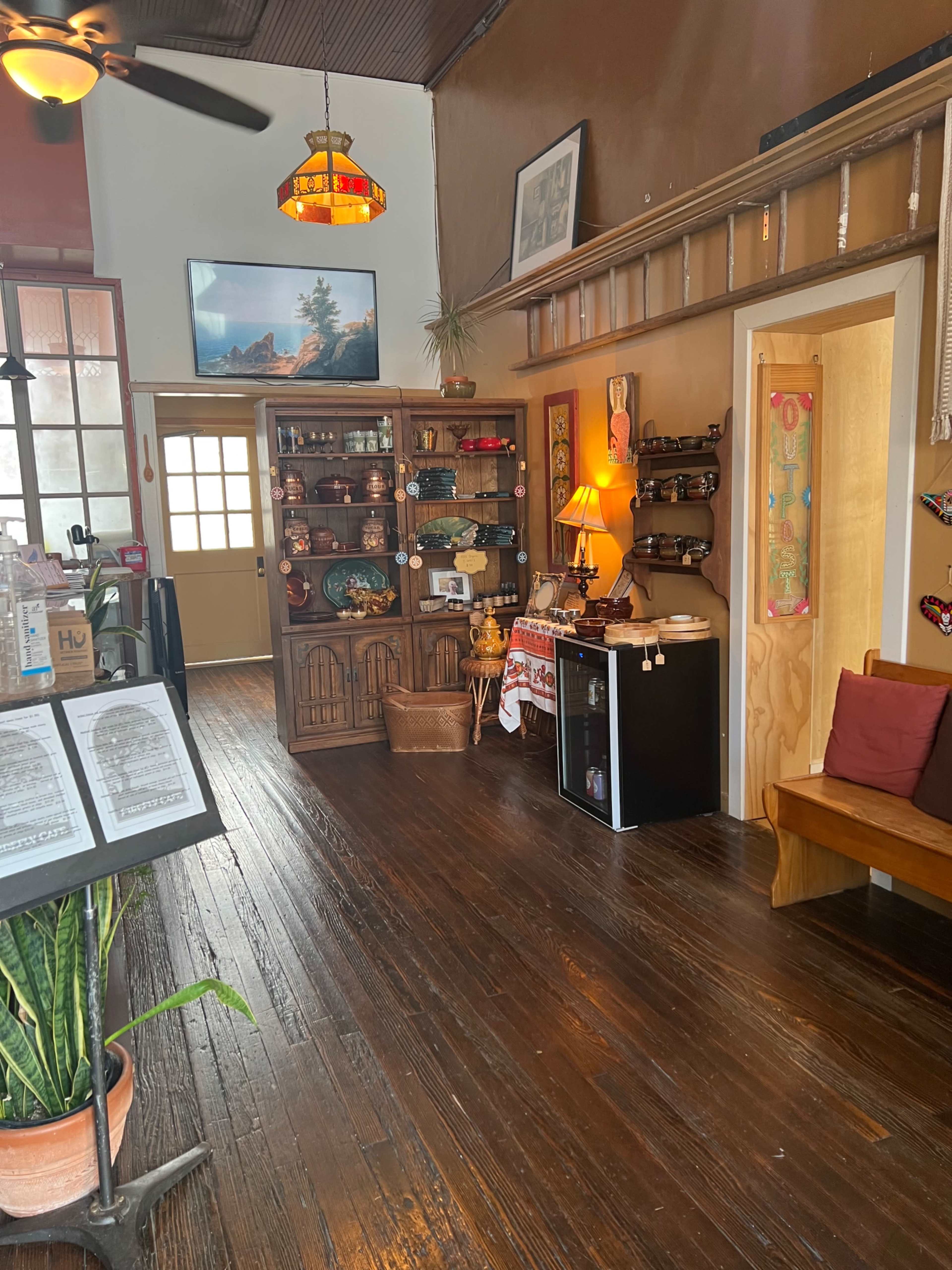 A cozy entryway with wooden floors, a bookshelf displaying decorative items, and a small refrigerator next to a lamp in a warmly lit room.