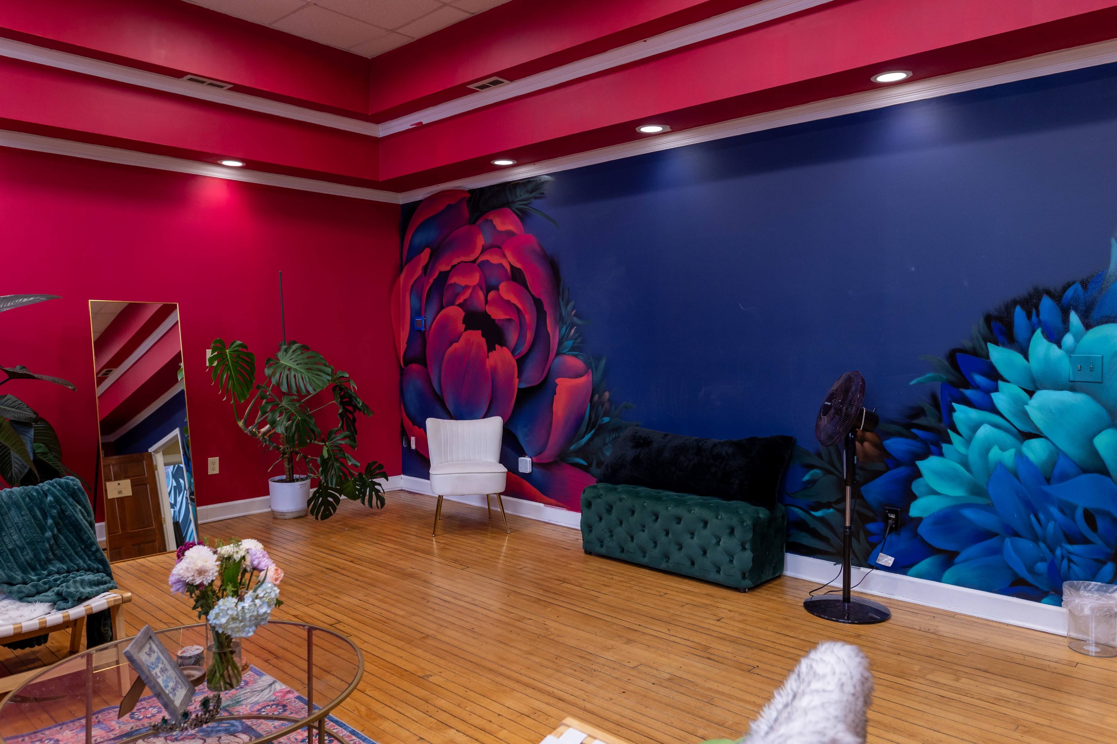 The image shows a vibrant interior space with a colorful floral mural on the wall, contrasting with the wood floor and a mix of modern furniture.