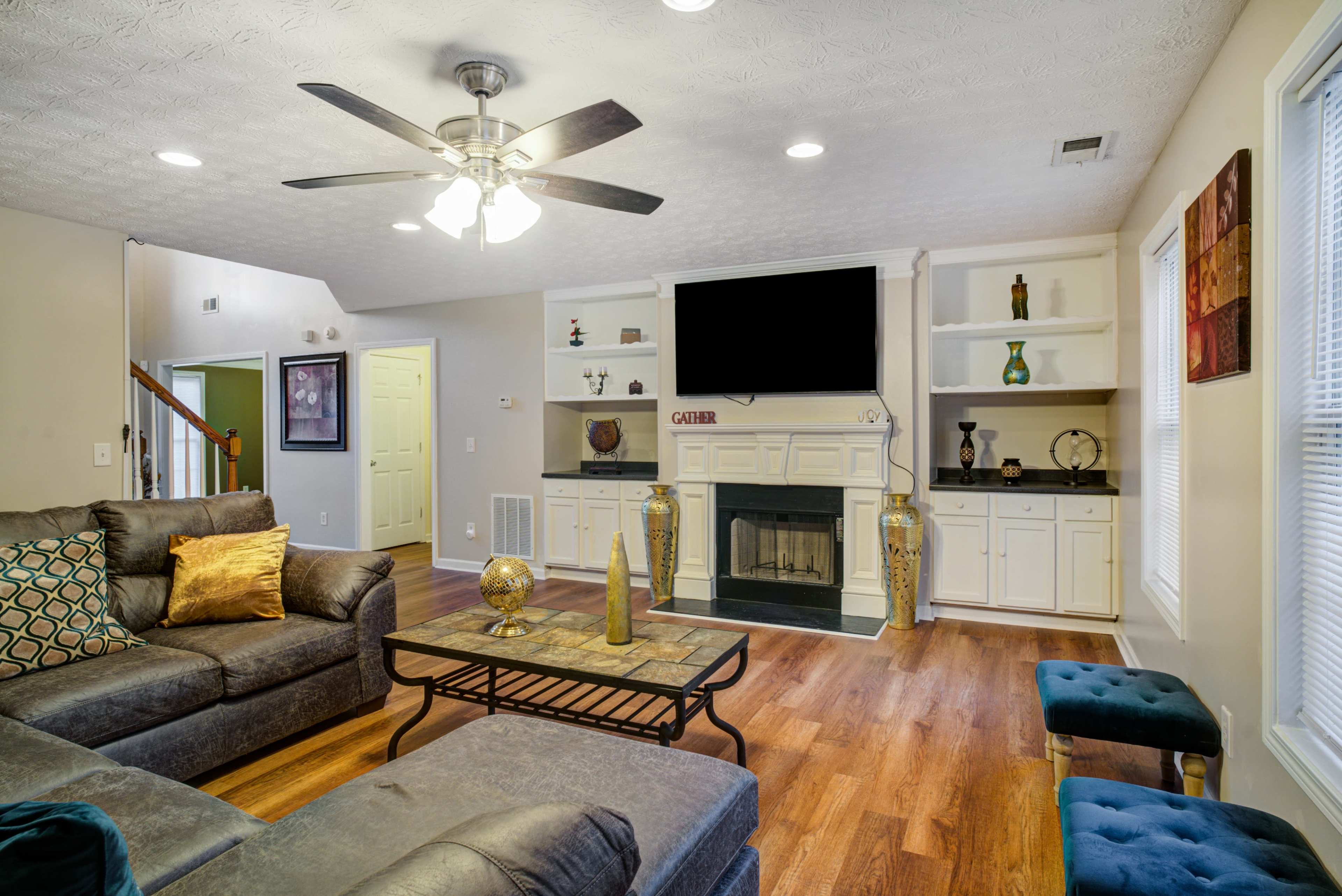 A living room with a sectional sofa, a coffee table, a fireplace, and built-in shelves, featuring a television mounted above the mantel.