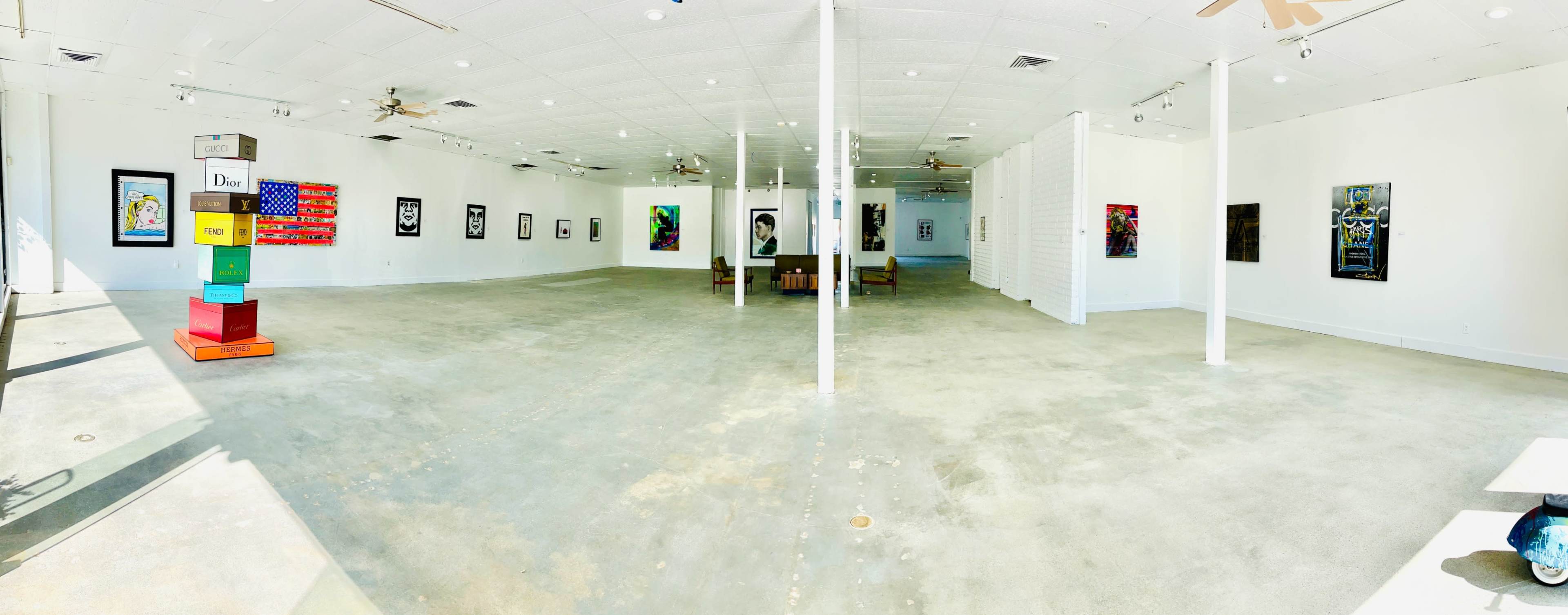 A spacious art gallery featuring rows of framed artworks on white walls and a simple arrangement of furniture in the center.