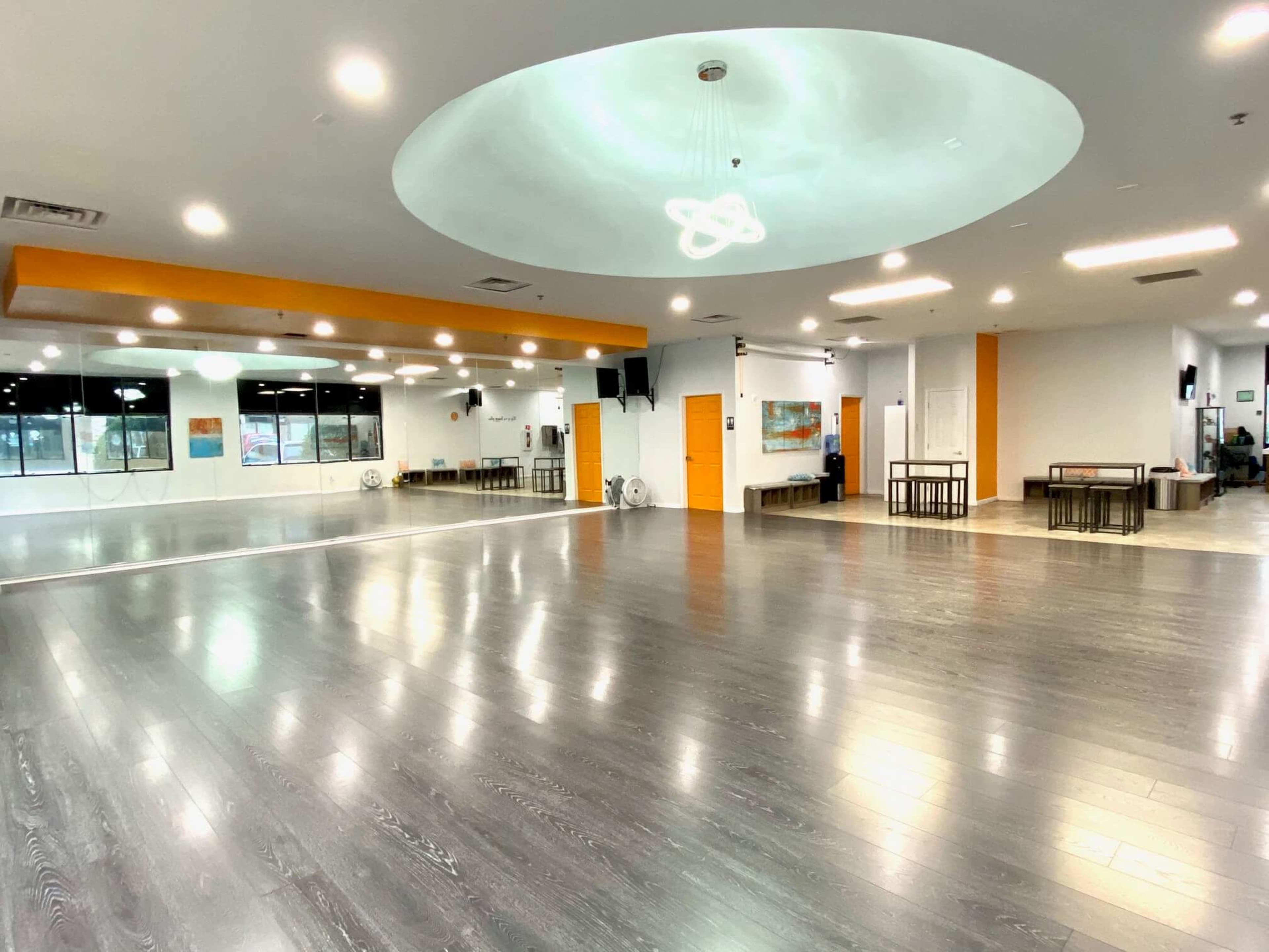A spacious, well-lit dance studio with a wooden floor, large mirrors, and minimal furniture.