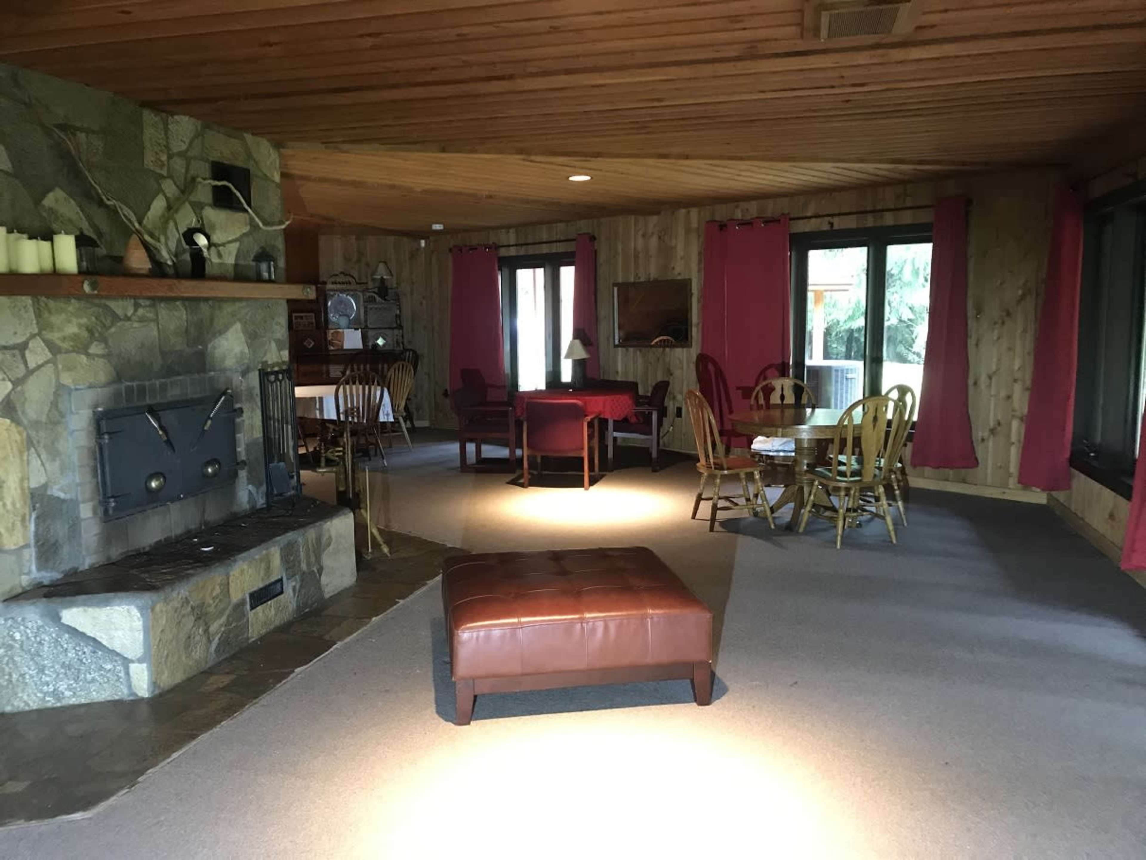 A spacious living area features a stone fireplace, a central ottoman, and a dining table surrounded by wooden chairs.