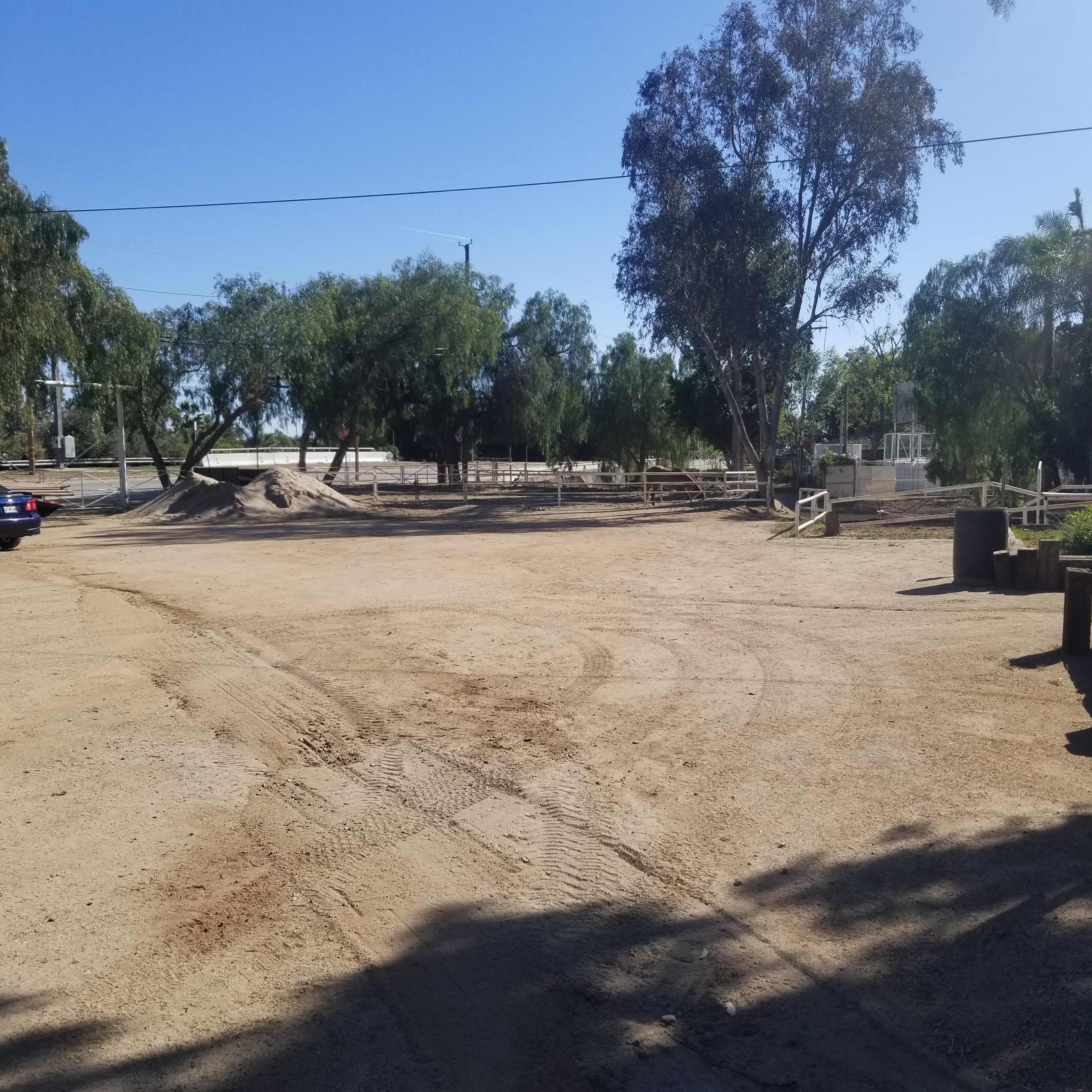 A sandy, open area with some trees and a pile of dirt, along with a parked car in the foreground.