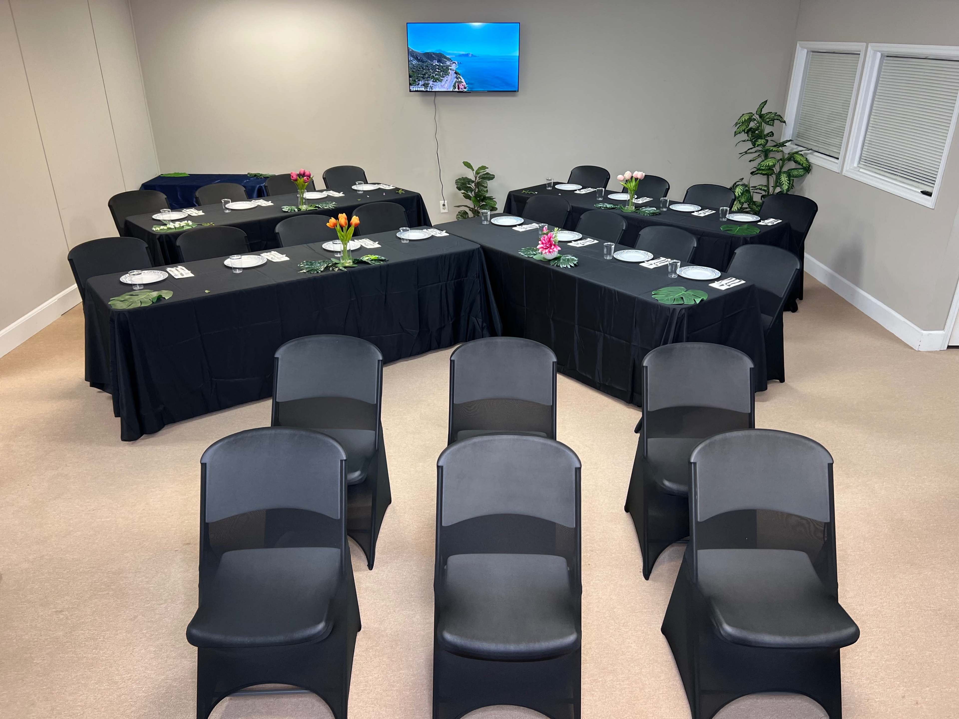 A meeting room is arranged with several tables covered in black cloth, set for a presentation, and black chairs facing the tables.