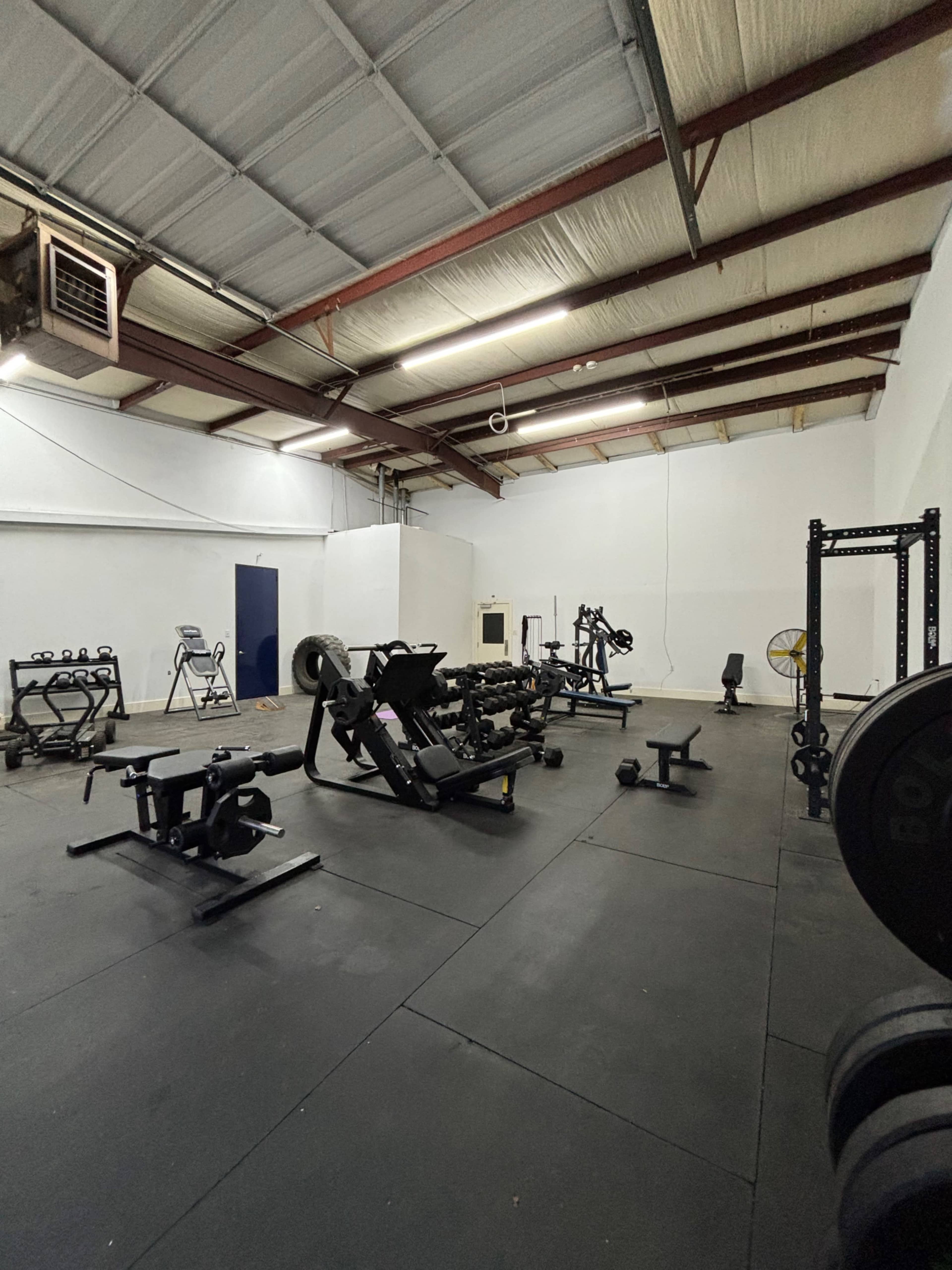 A spacious gym filled with various weightlifting equipment and exercise machines on a rubber flooring surface.