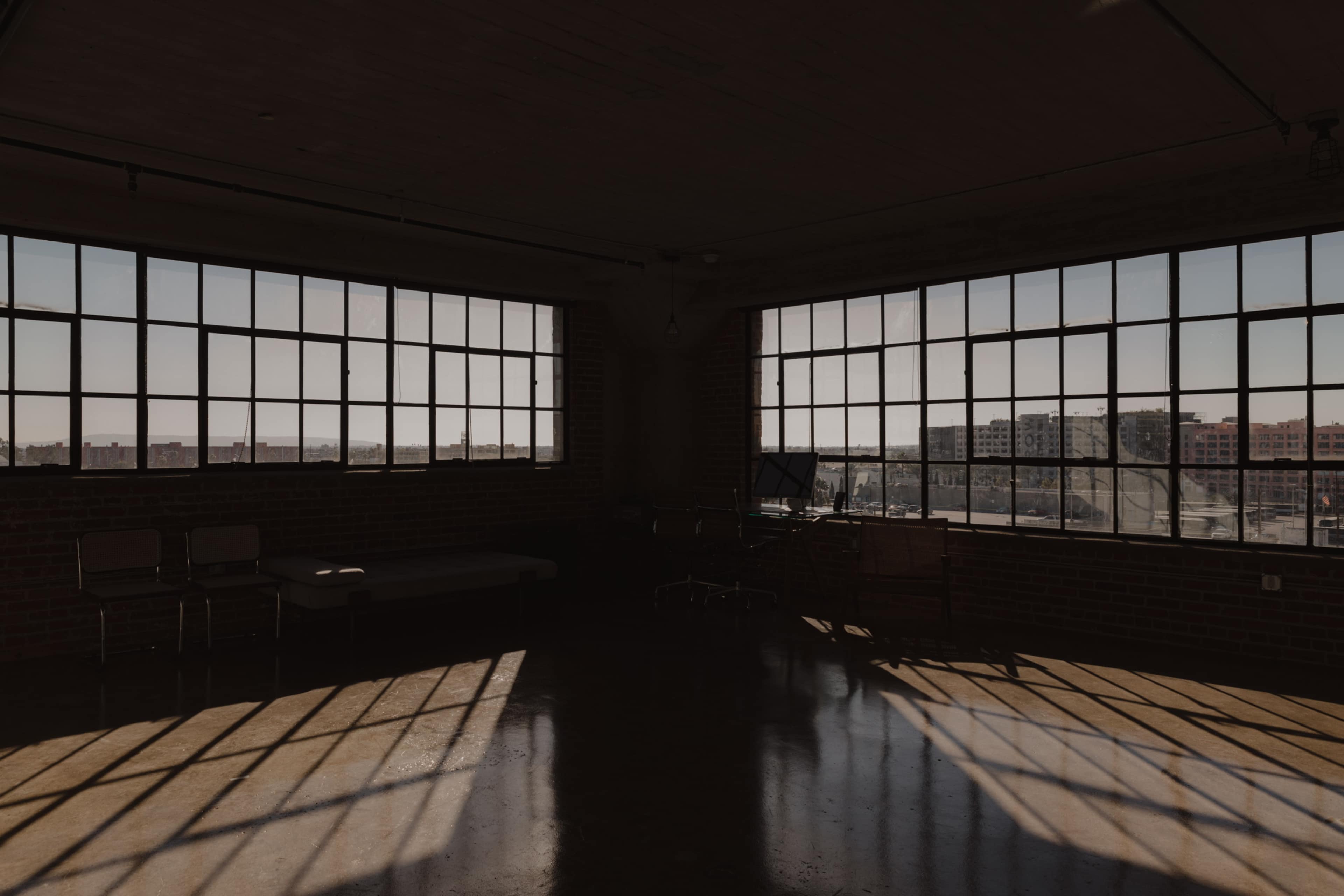 A dimly lit industrial space with large windows allowing sunlight to cast shadows on the polished floor.