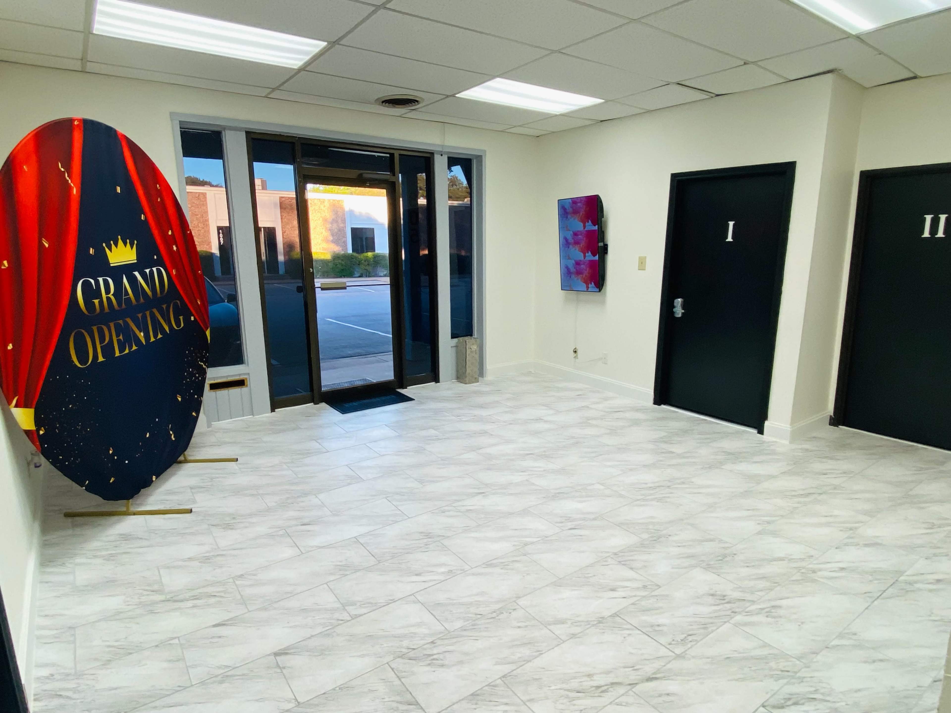 The image shows a spacious entrance lobby with a large circular sign displaying "GRAND OPENING" and two black doors labeled "I" and "II."