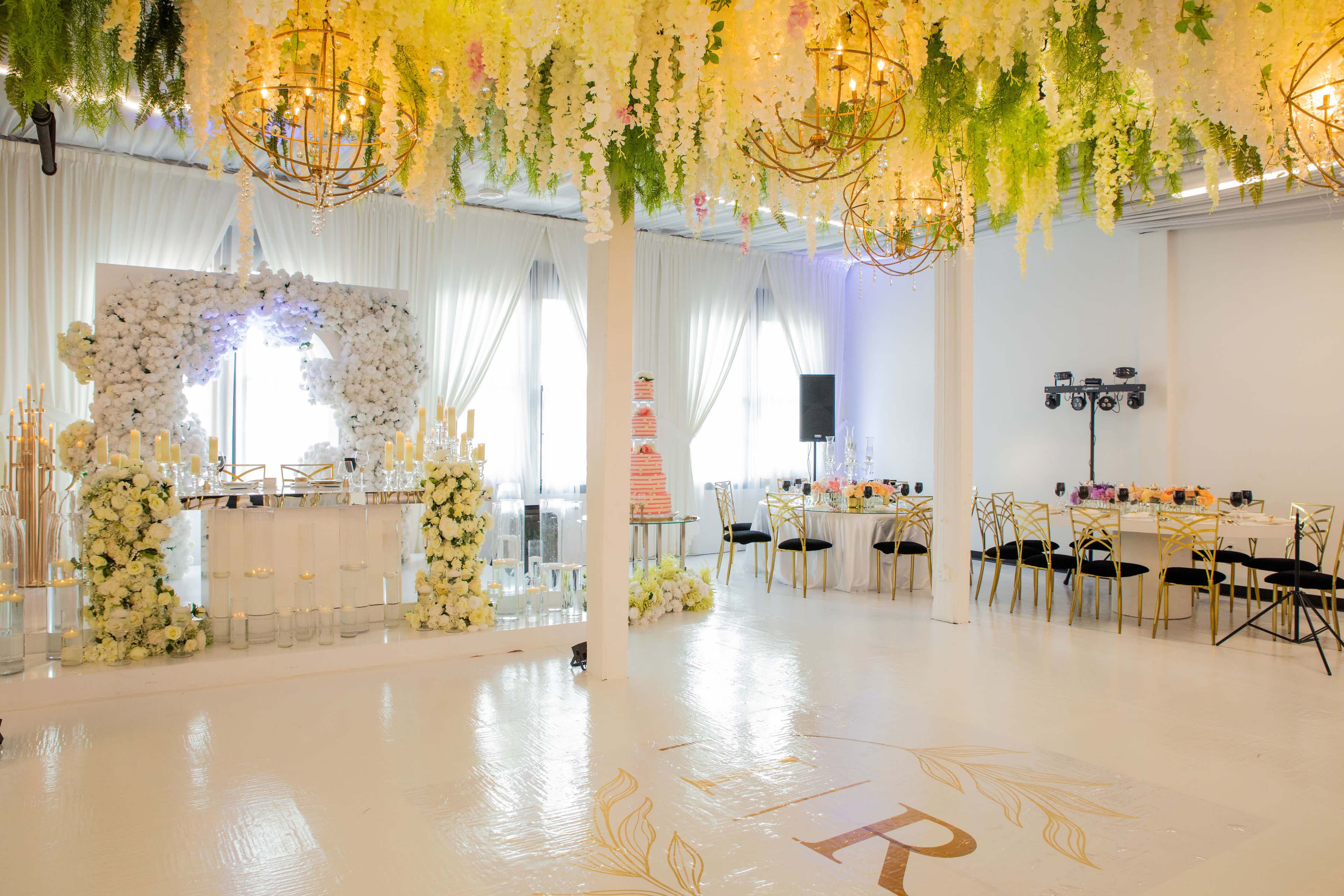 A beautifully decorated event space with floral arrangements hanging from the ceiling, a cake display, and elegantly set tables.