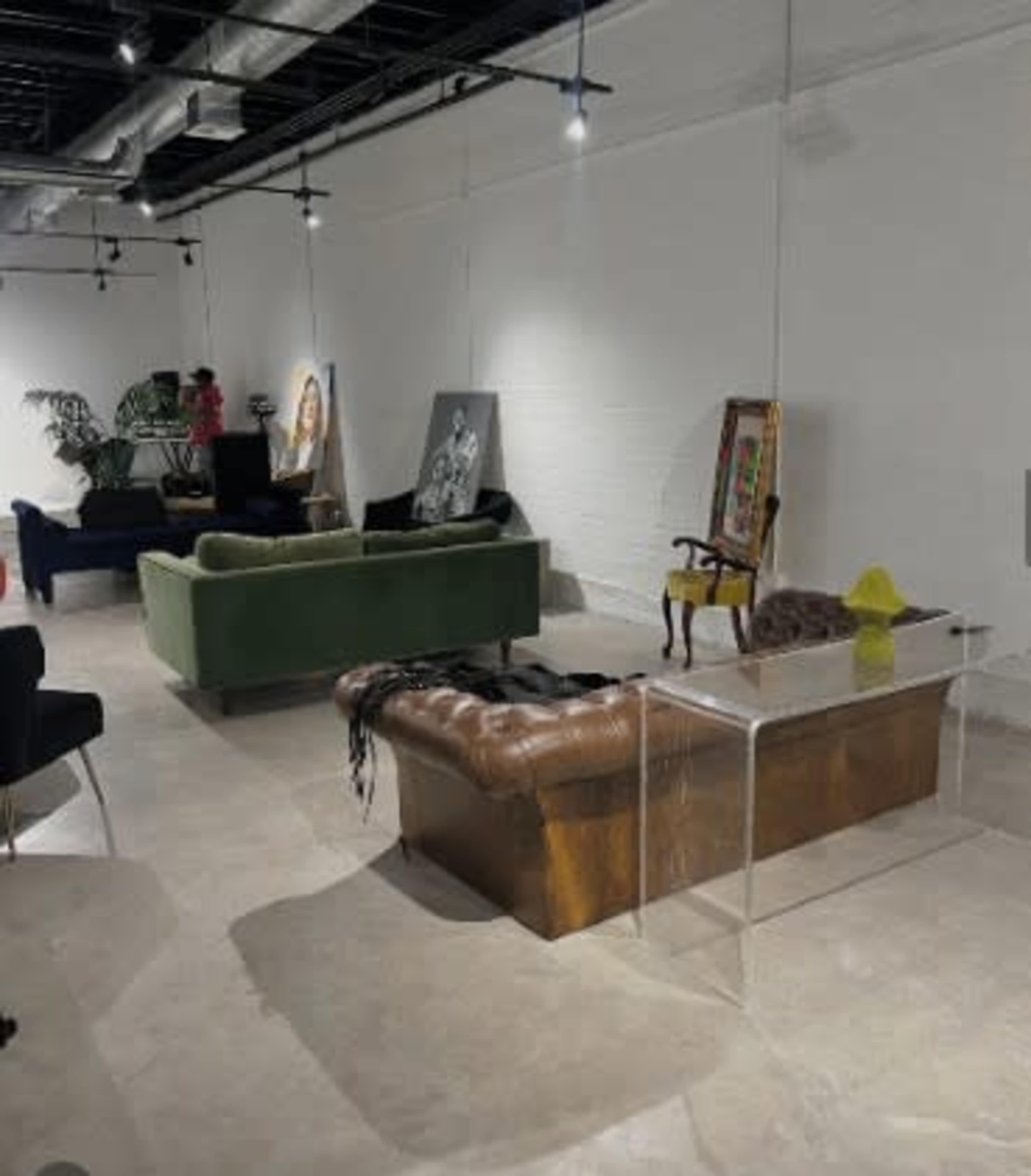The image shows a modern interior space furnished with various couches, an acrylic coffee table, and artwork displayed on the walls.