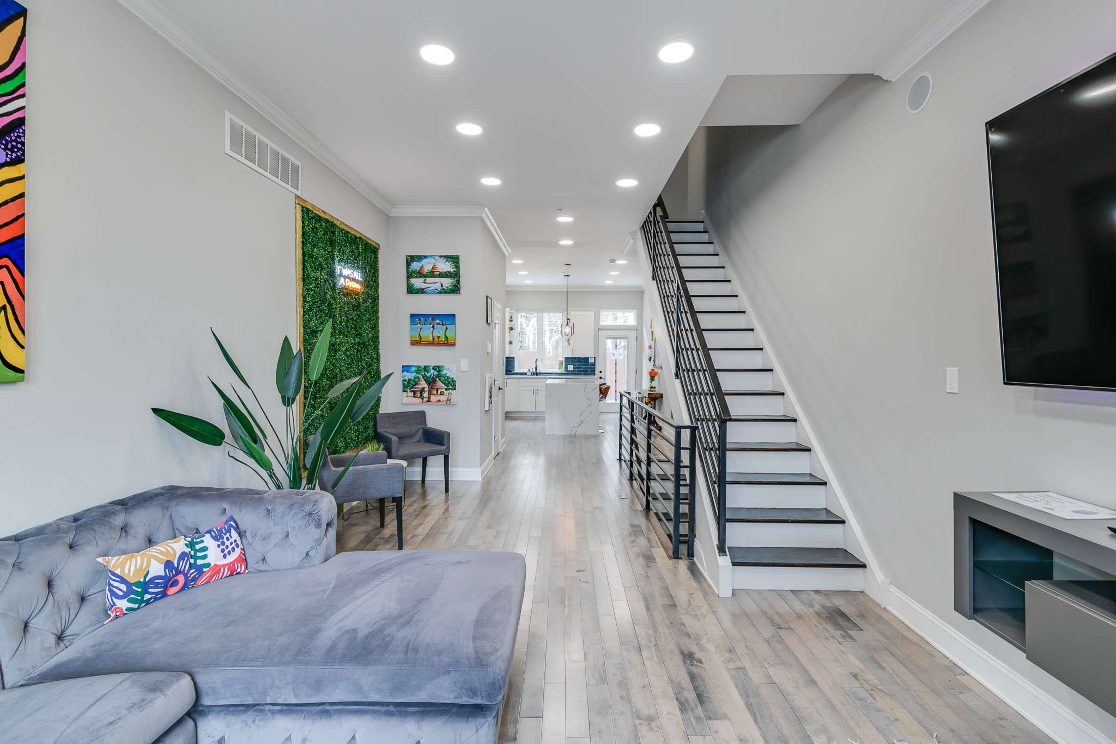 A modern living space with grey furniture, a staircase leading to an upper level, and a bright open kitchen area visible in the background.