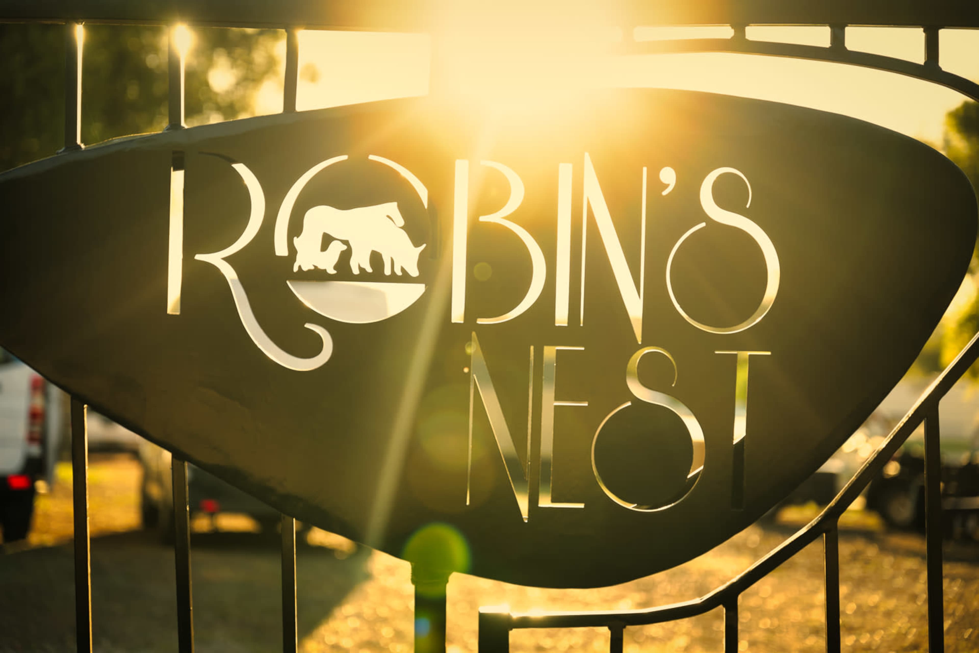 A wrought iron sign that reads "Robin's Nest," with a silhouette of a horse, illuminated by sunlight in the background.