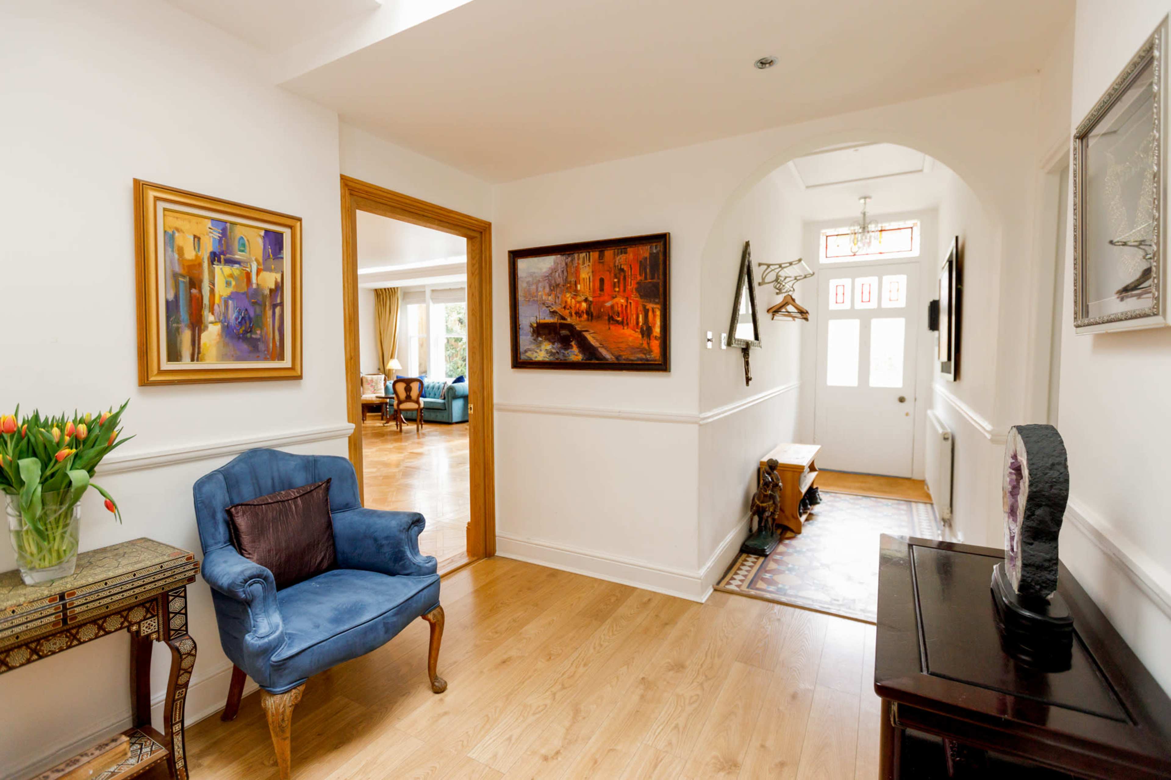 A bright hallway features a blue chair, framed artwork on the walls, and a door that leads outside.