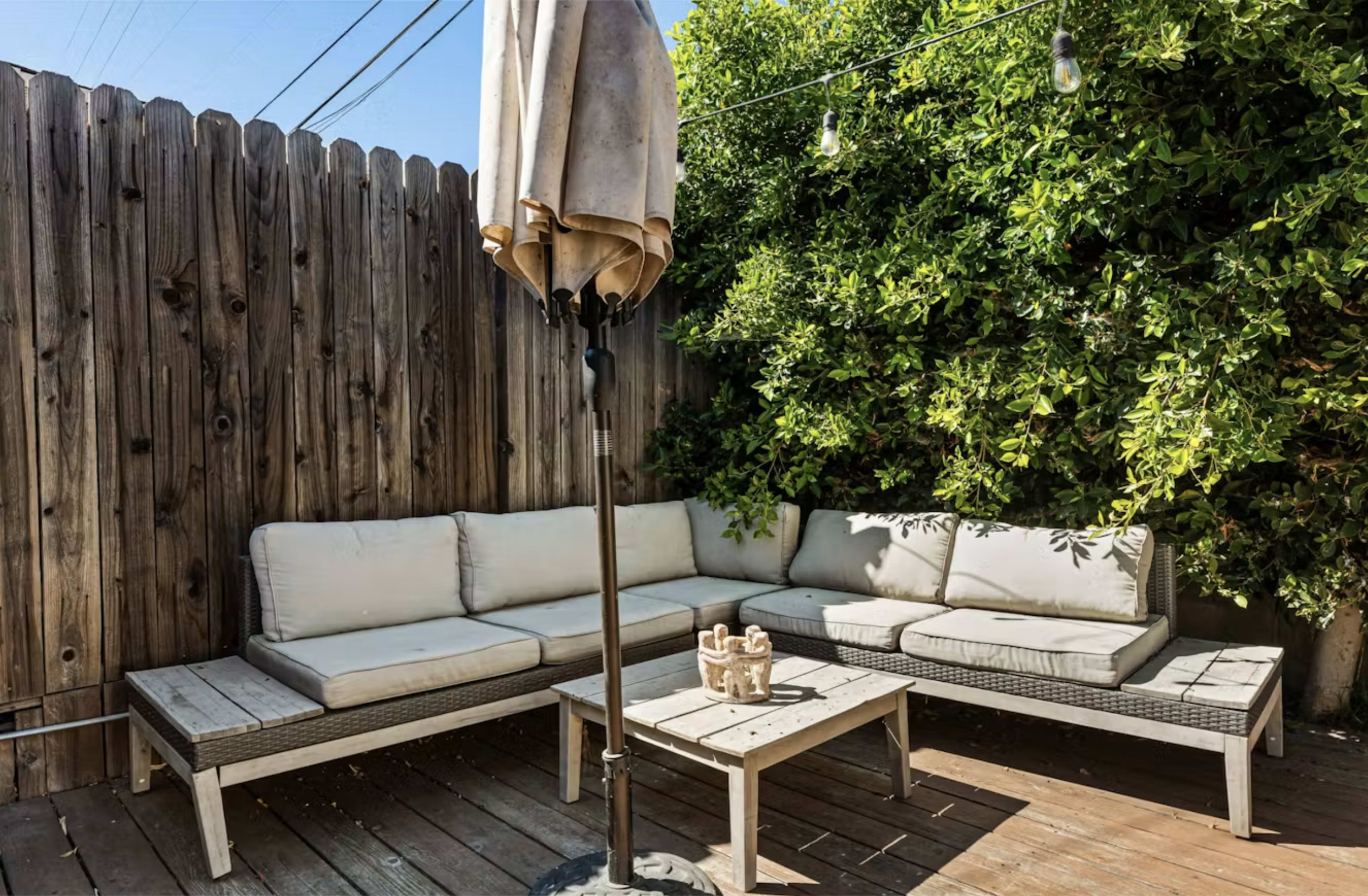 A patio area features a sectional sofa and a small table, surrounded by a wooden fence and greenery.
