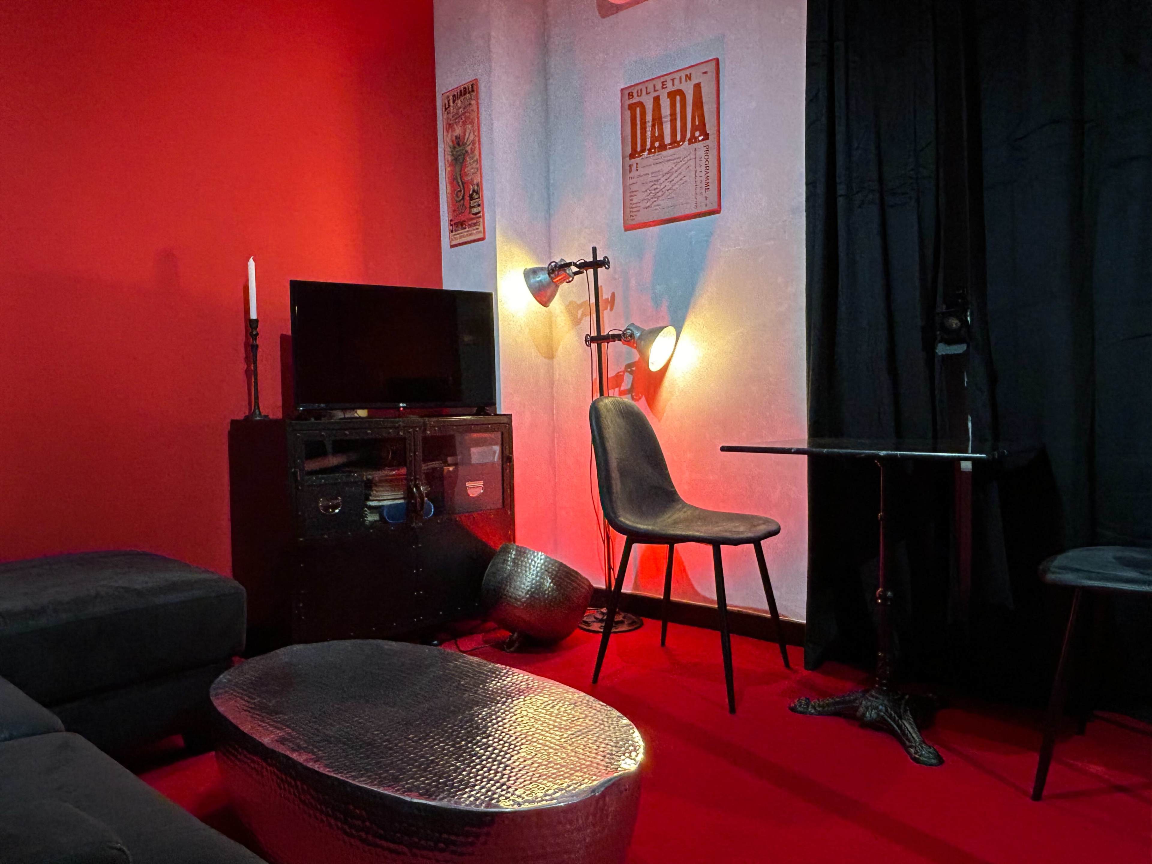 The image shows a room with red walls, a small table, a chair, a television, and ambient lighting.