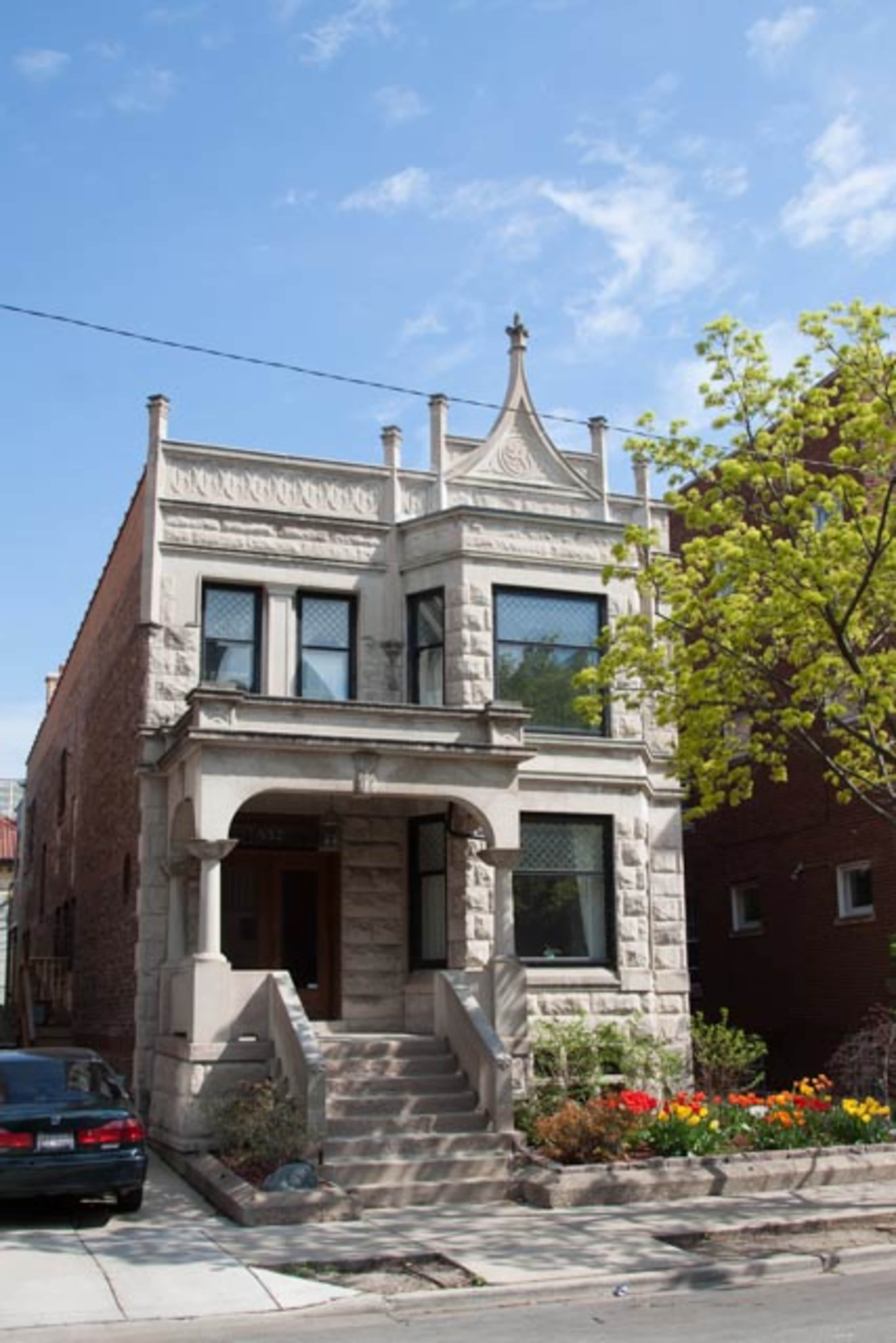 A two-story stone house with decorative elements and a small garden in front.