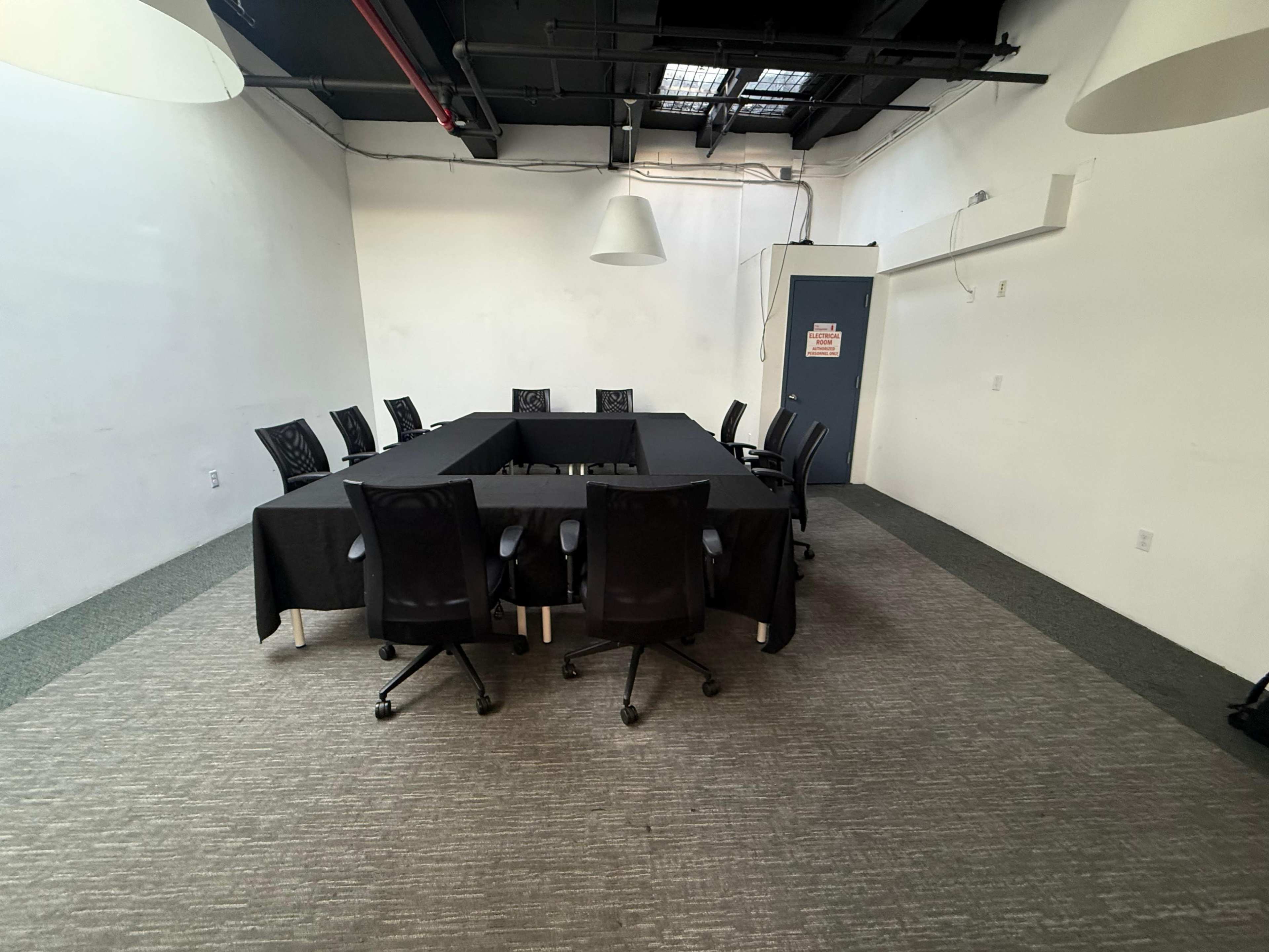 A rectangular conference room features a large table surrounded by black chairs, with a door visible on one side.