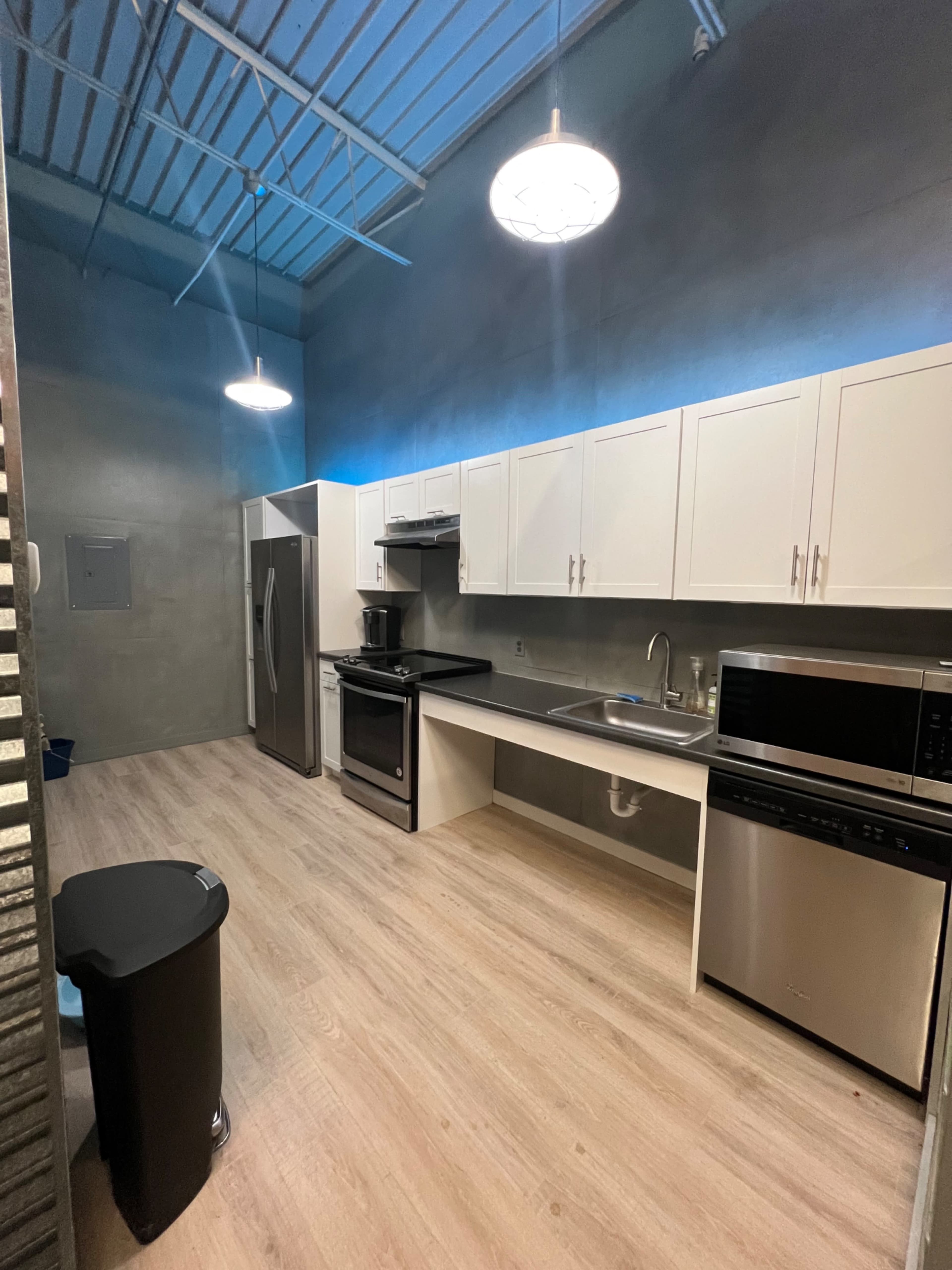 A modern kitchen with white cabinets, stainless steel appliances, and a light wood floor.