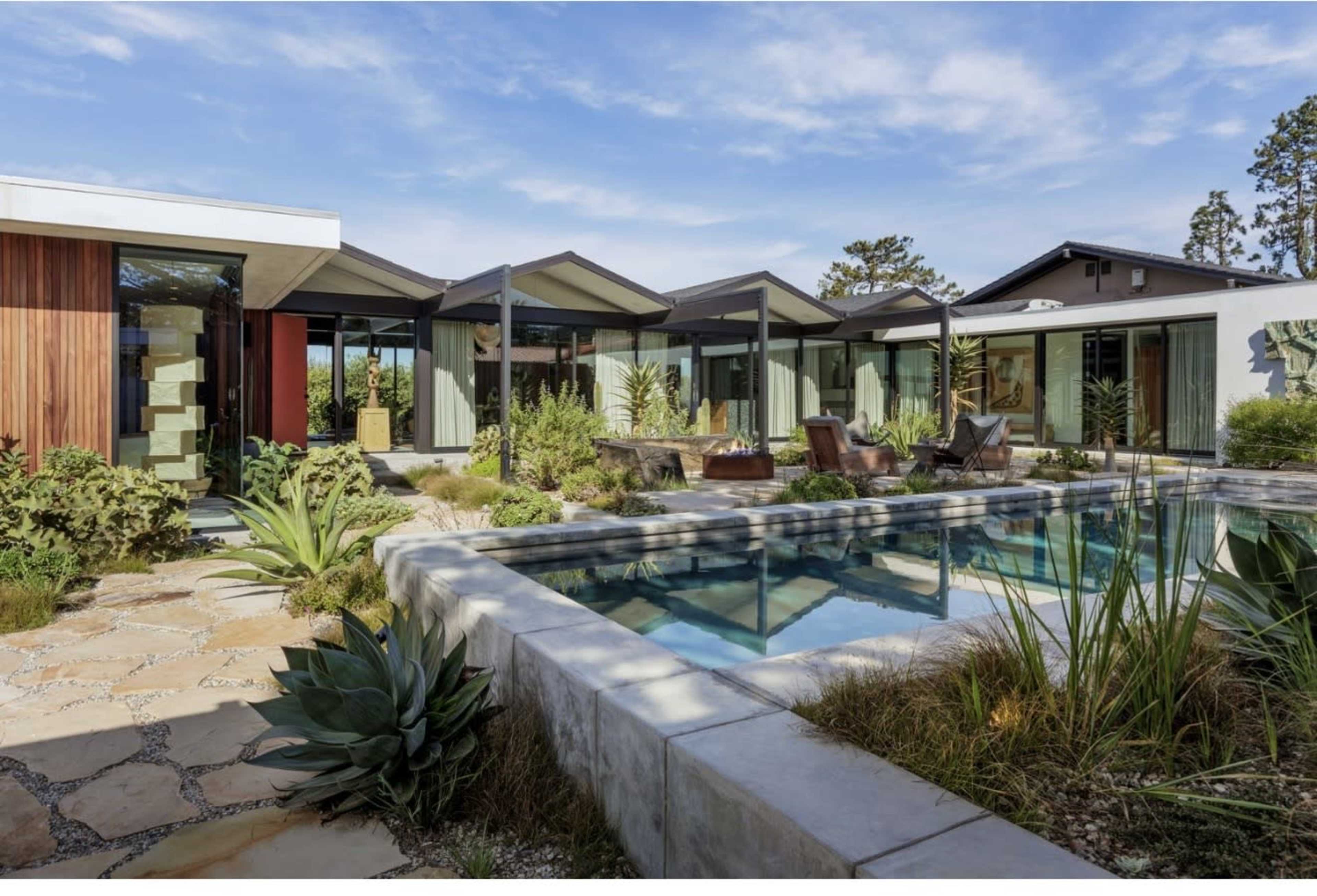 The image shows a modern architectural residence with large glass windows surrounding a swimming pool and landscaped garden.