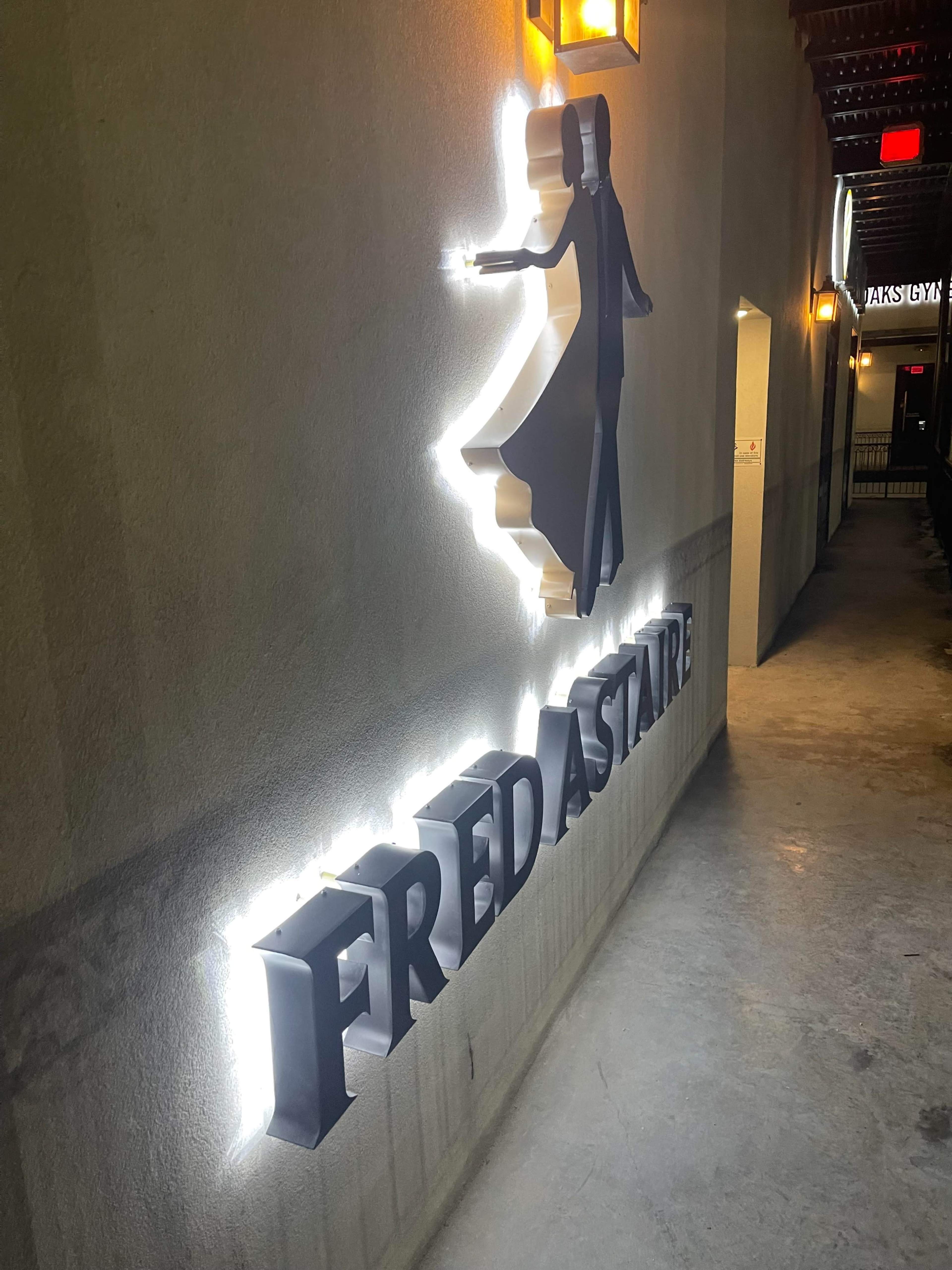 A backlit sign reading "FRED ASTAIRE" along a wall, accompanied by a silhouette of a dancing couple.